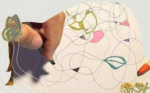 Child's hand drawing with a marker on a piece of paper with colorful scribbles and doodles, including a butterfly perched on the child's hand.