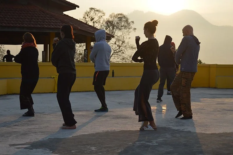 People practicing yoga on a rooftop during sunrise or sunset.