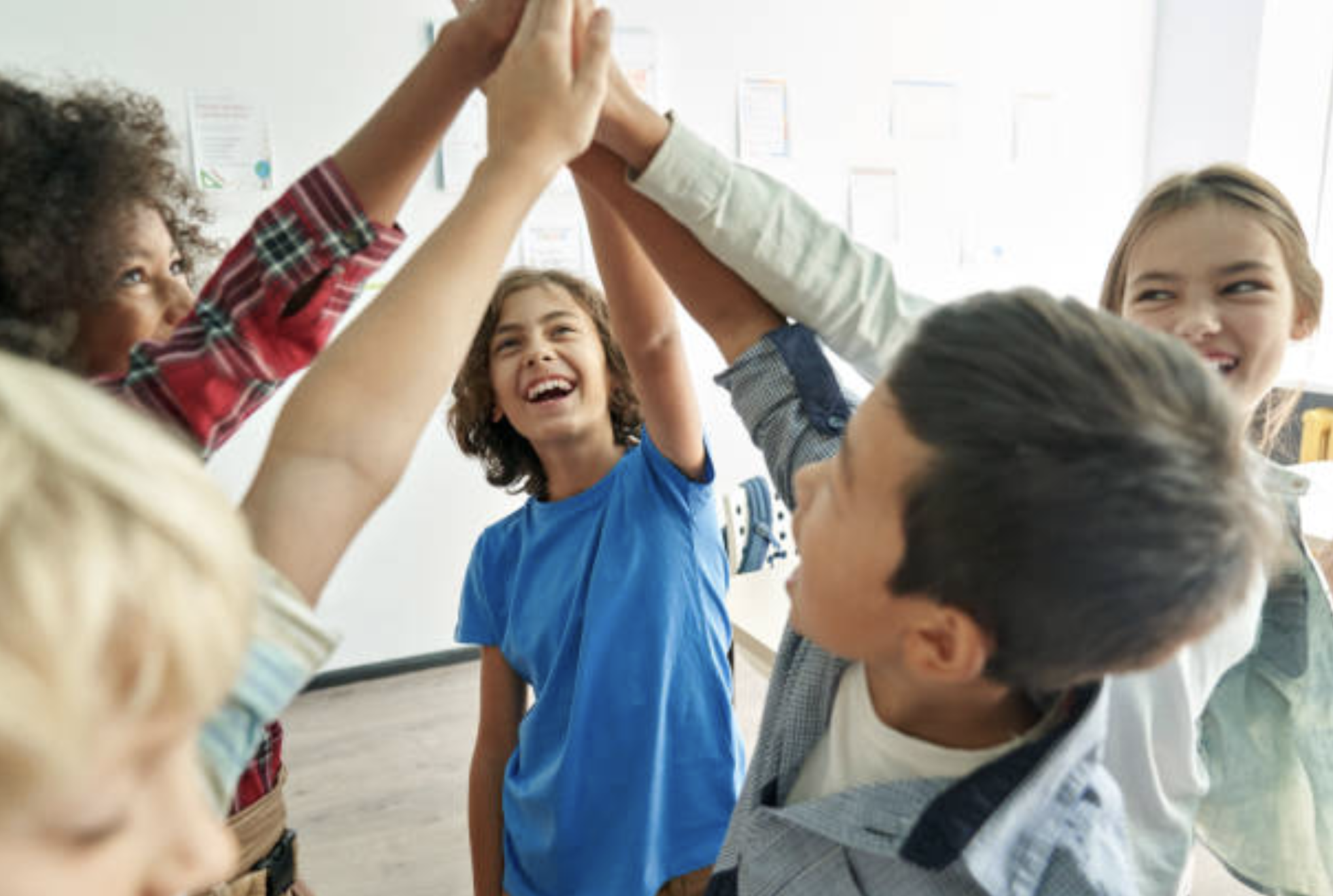 Group of diverse children in a classroom giving high five together, smiling and laughing.