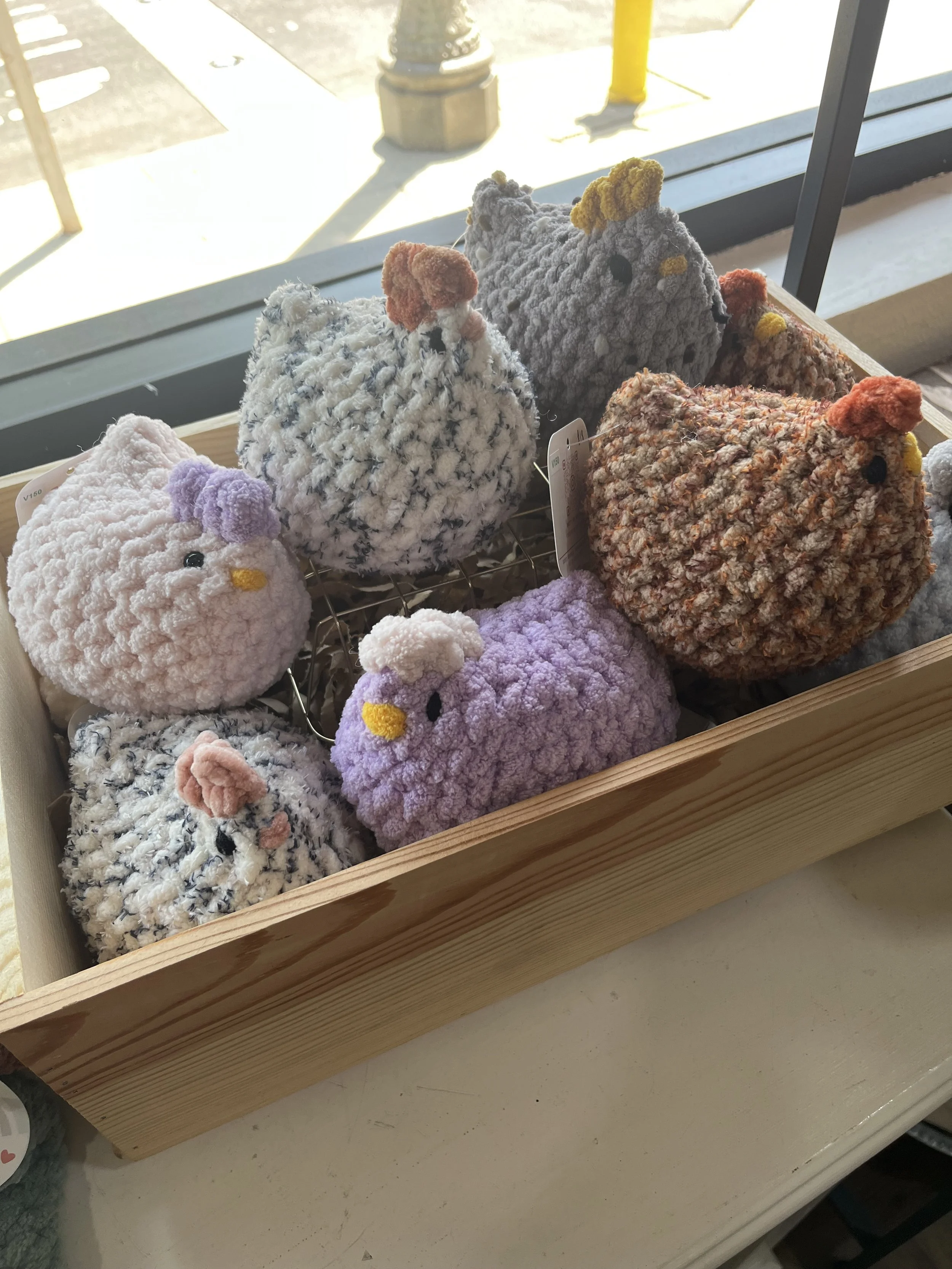 Handmade plush crochet chickens in assorted colors, displayed in a wooden crate. Cute and cozy décor or gift items available at Rustic and Modern Collective in Upland, CA.