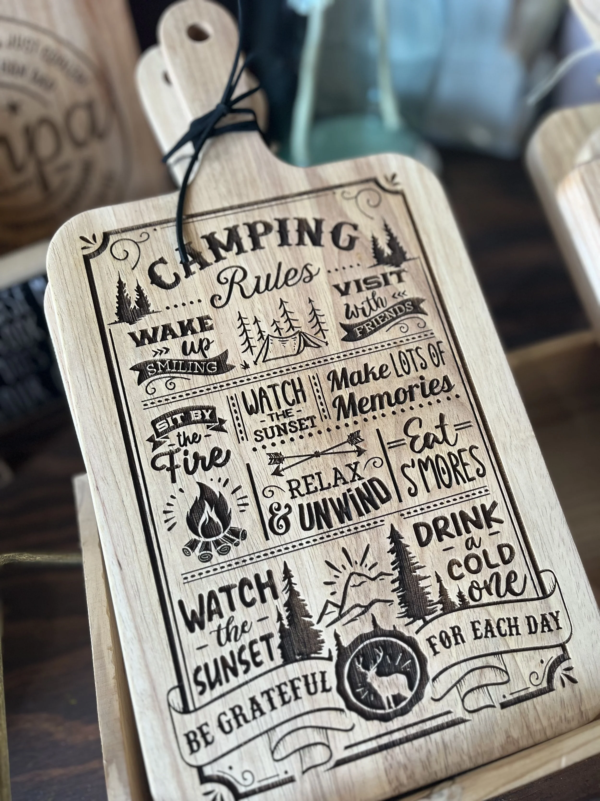 Wooden cutting board engraved with “Camping Rules” design, featuring fun reminders like sit by the fire, eat s’mores, relax and unwind, and watch the sunset. Available at Rustic and Modern Collective in Upland, CA.