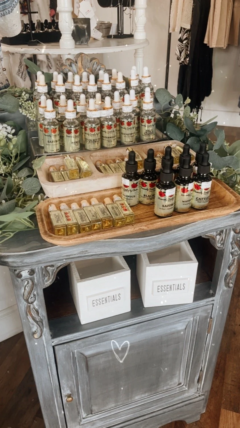 Display of essential oils and fragrances on a rustic wooden table with greenery decoration, in a boutique store setting.