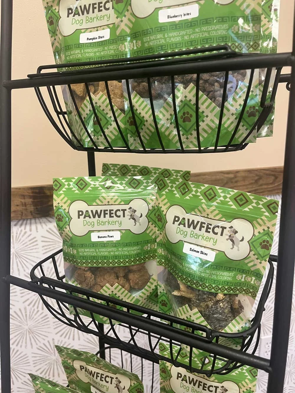 Display shelf with packaged dog treats labeled 'PAWFECT Dog Barkery' in green, with flavors like 'Banana Paws' and 'Salmon Skins.'