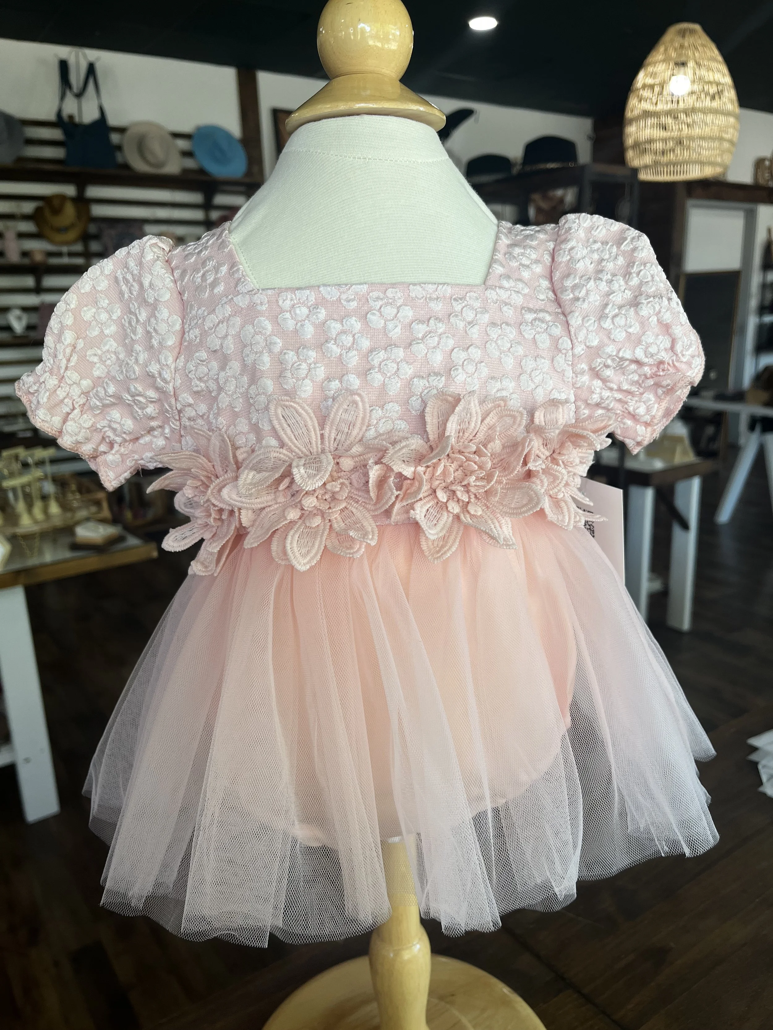 Baby pink floral lace dress with puff sleeves, 3D flower appliqué waist, and soft tulle skirt displayed on a mannequin at Rustic and Modern Collective