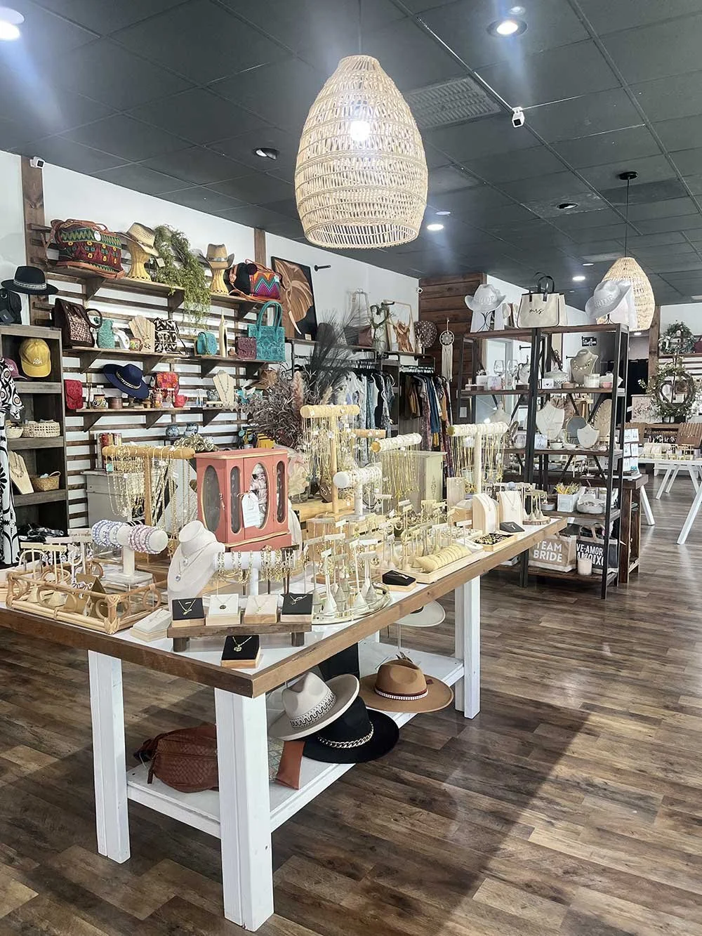 Interior of a boutique retail store with displays of hats, jewelry, handbags, and accessories, featuring wooden floors, pendant lighting, and wall shelves showcasing various items.