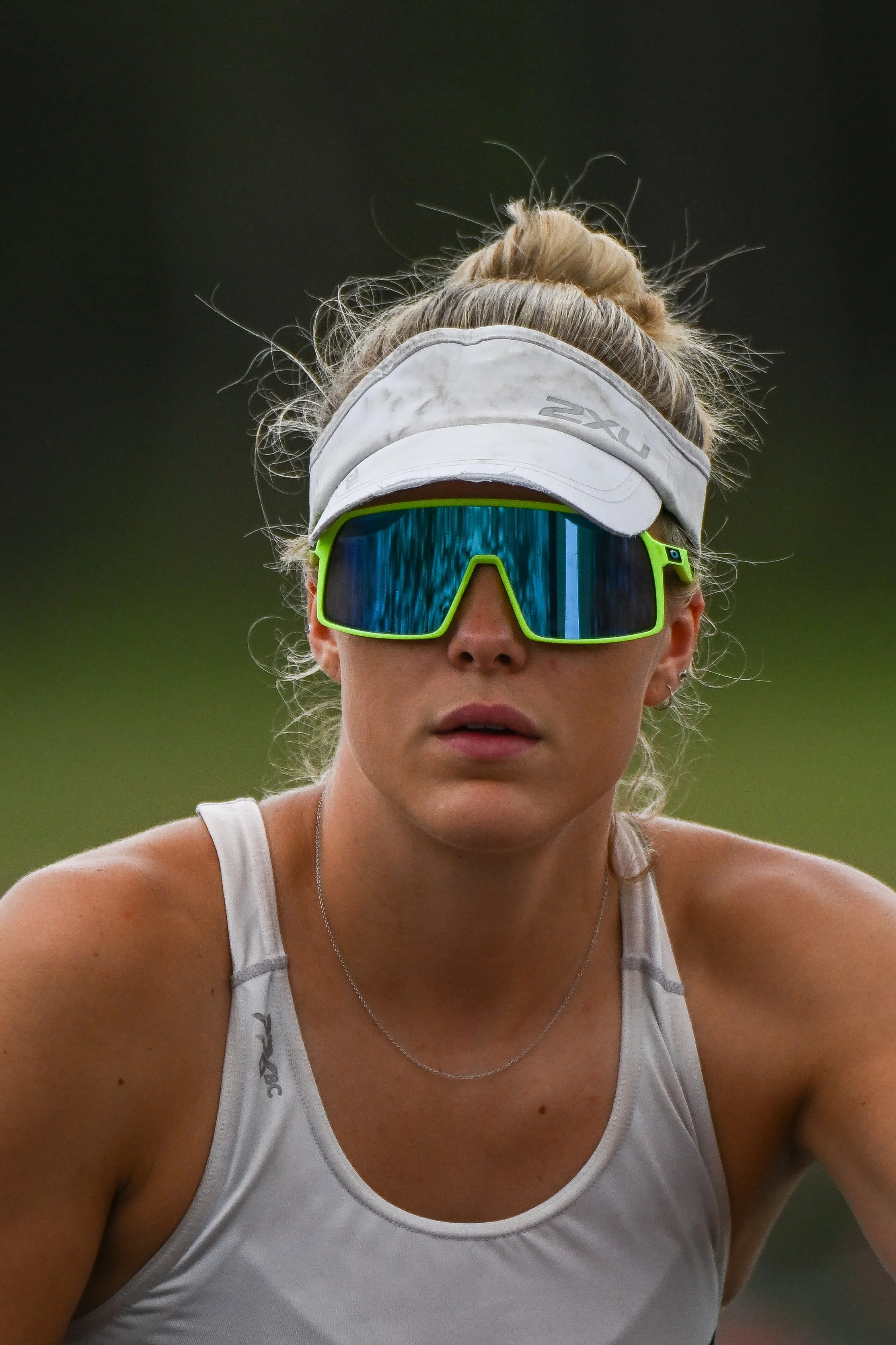 A female athlete outdoors wearing sunglasses, a visor, and athletic attire.