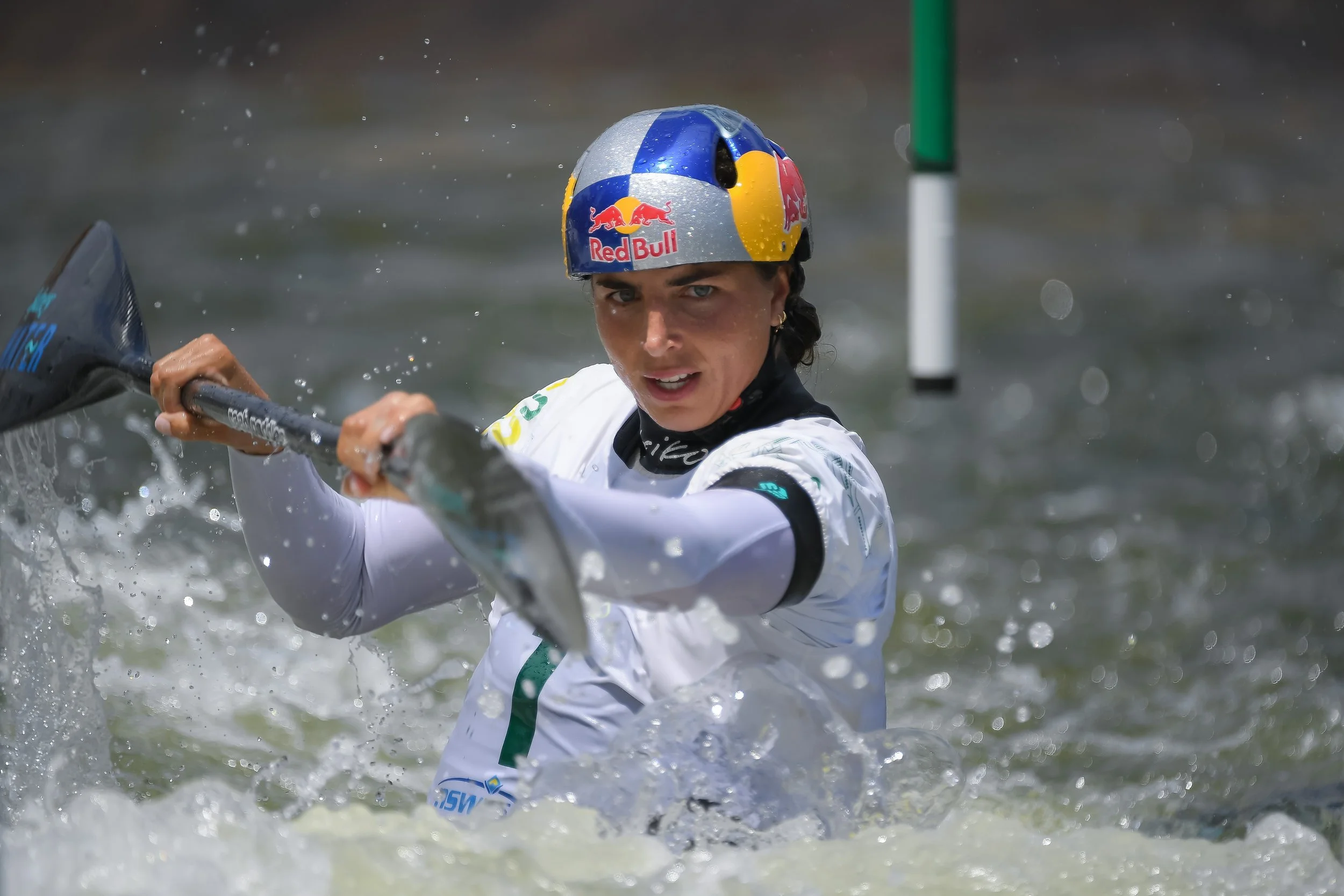 Female kayaker wearing a helmet with the Red Bull logo, paddling through a water course during a race.