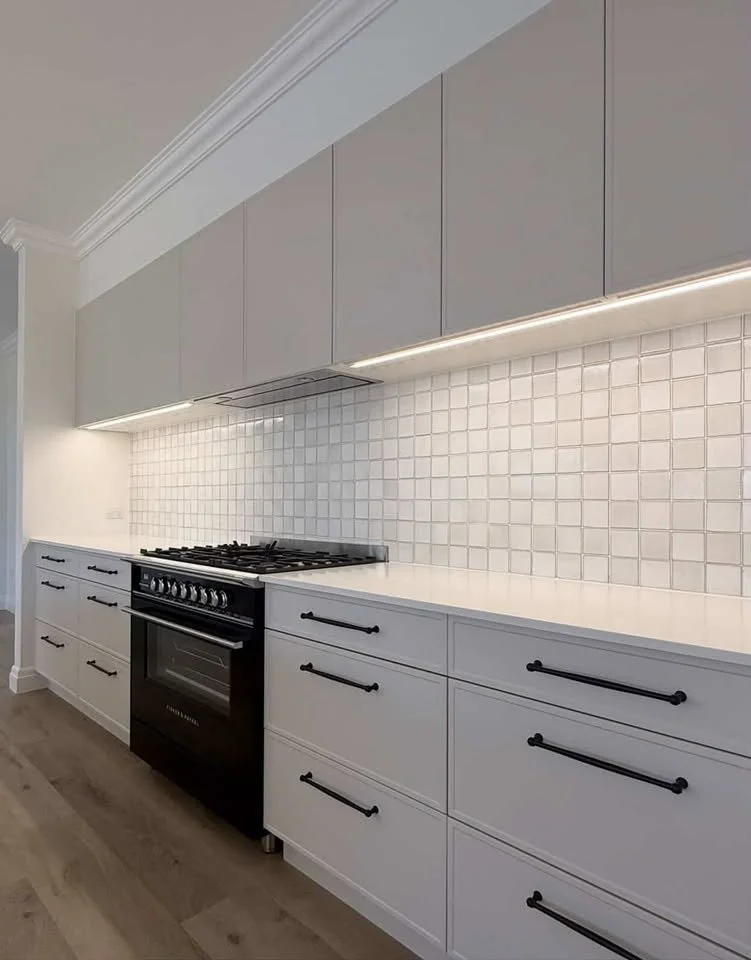 Modern kitchen with white cabinets, black handles, a black oven, and a white tiled backsplash.