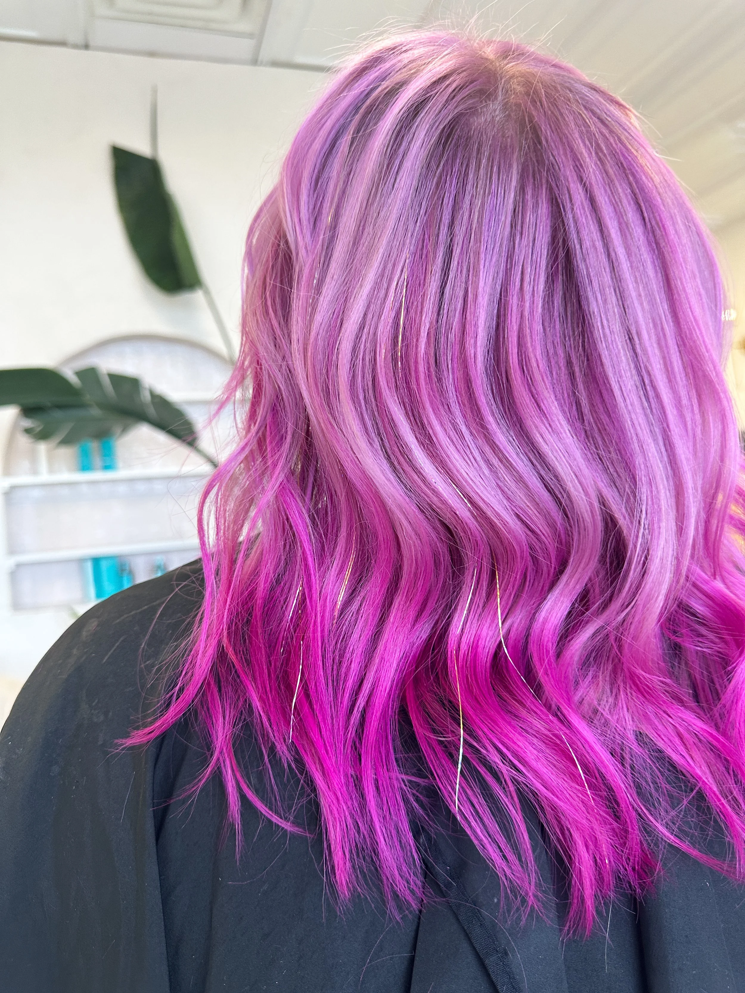 Back view of a person with long wavy hair dyed in shades of pink and purple.