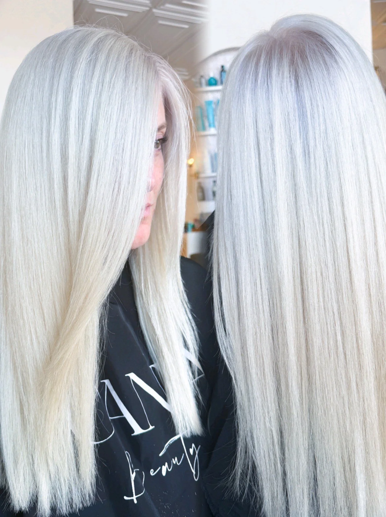 Side view of a woman with long, straight, platinum blonde hair looking into a mirror in a salon.