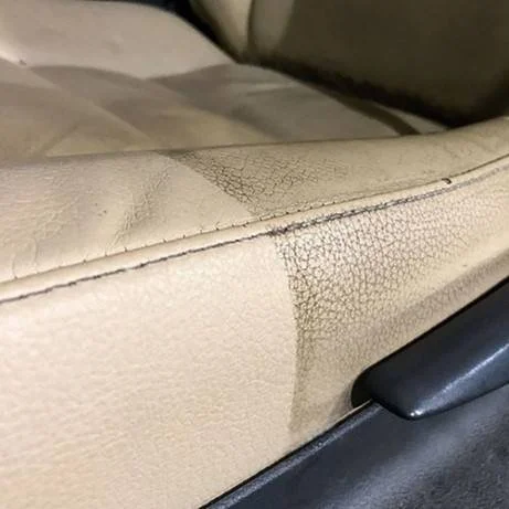 Close-up of a beige leather car seat with visible wear and tear, showing creases and discoloration.