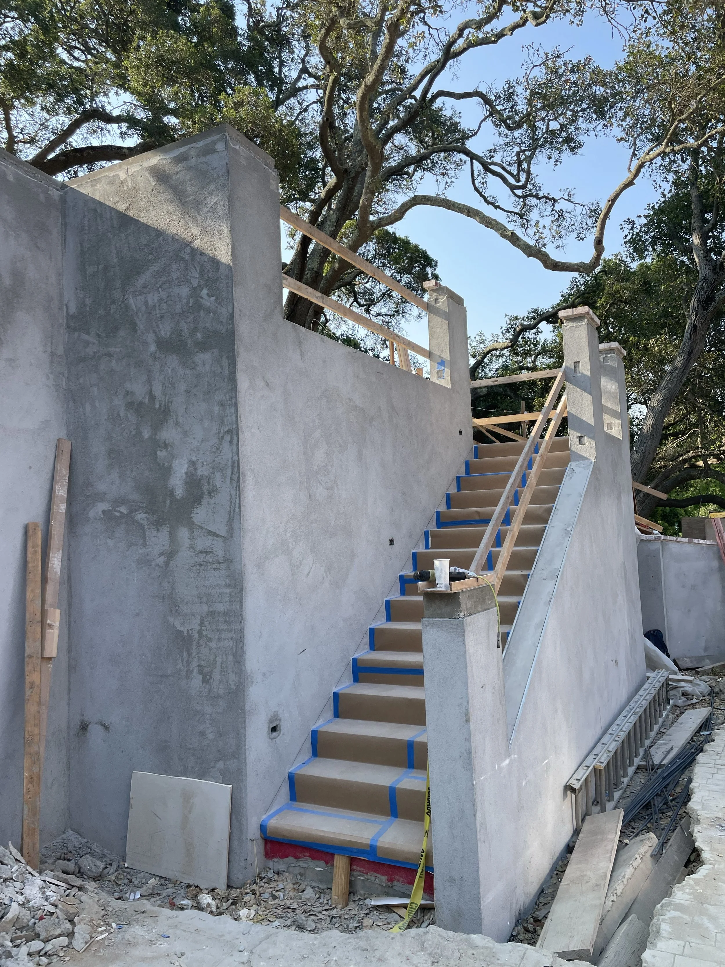 Outdoor concrete staircase under construction with surrounding debris and trees in the background.