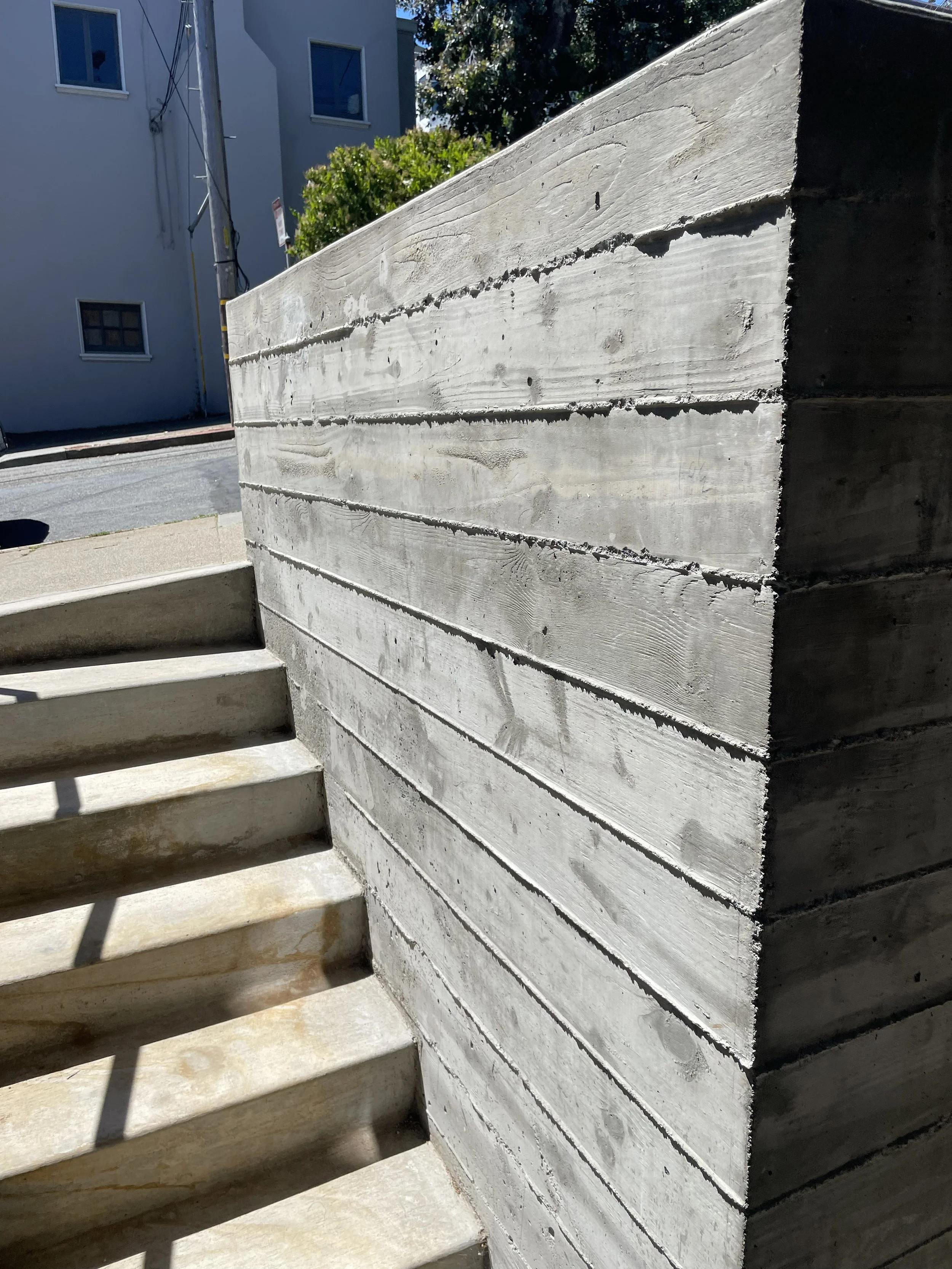 Concrete steps beside a textured concrete wall in an outdoor urban setting.