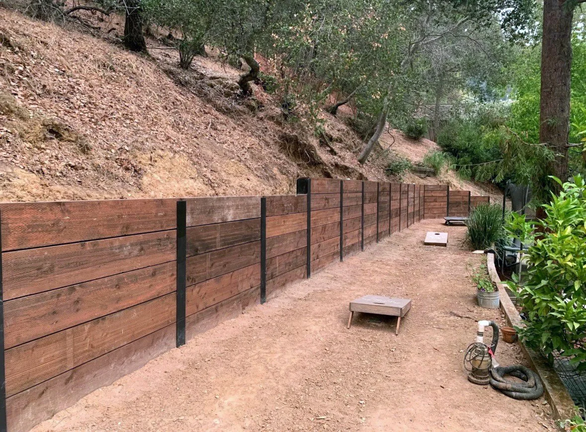 Wooden retaining wall on a dirt pathway with surrounding trees and plants.