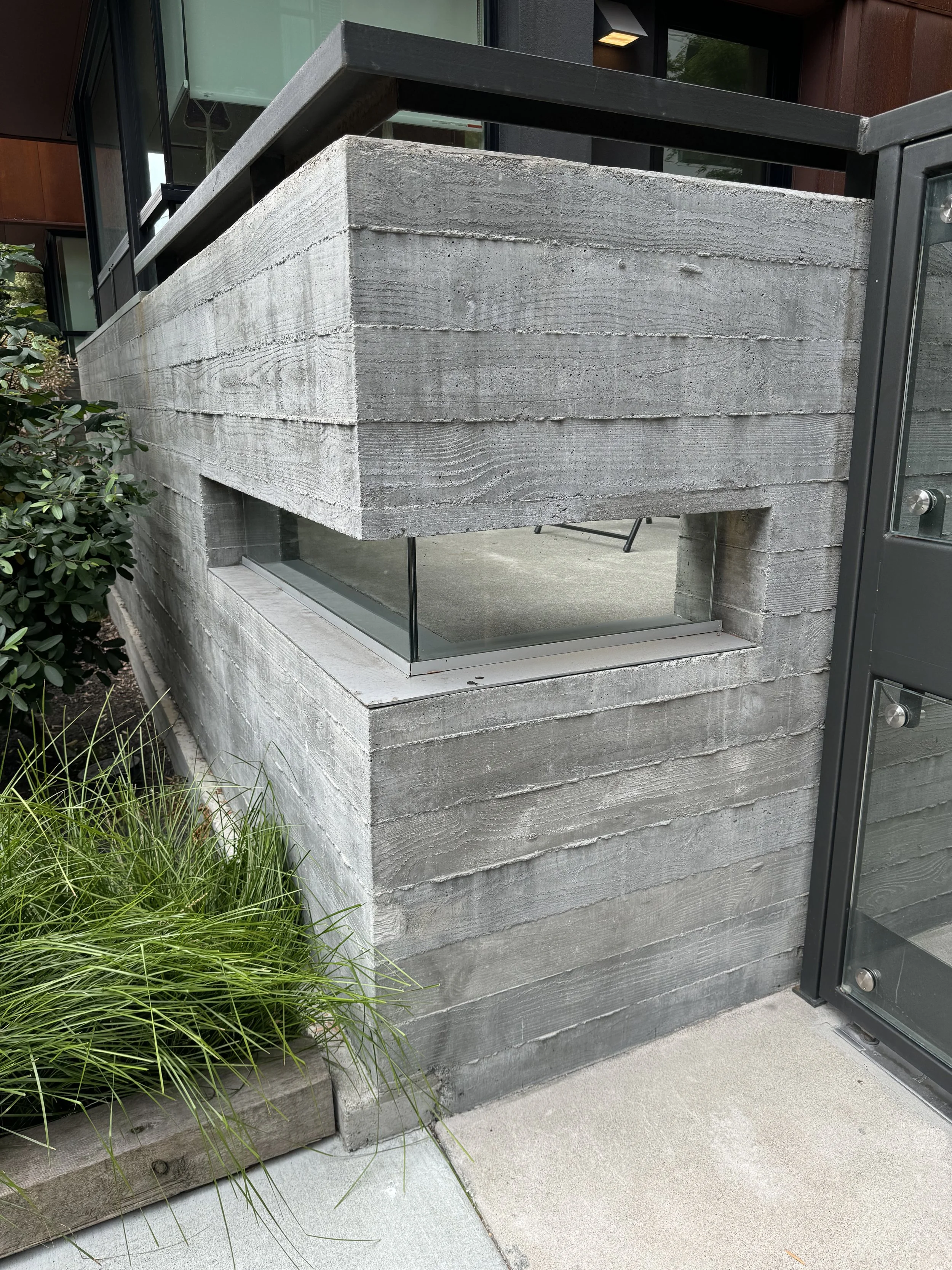 Modern concrete wall with a narrow window near a small garden and pathway.