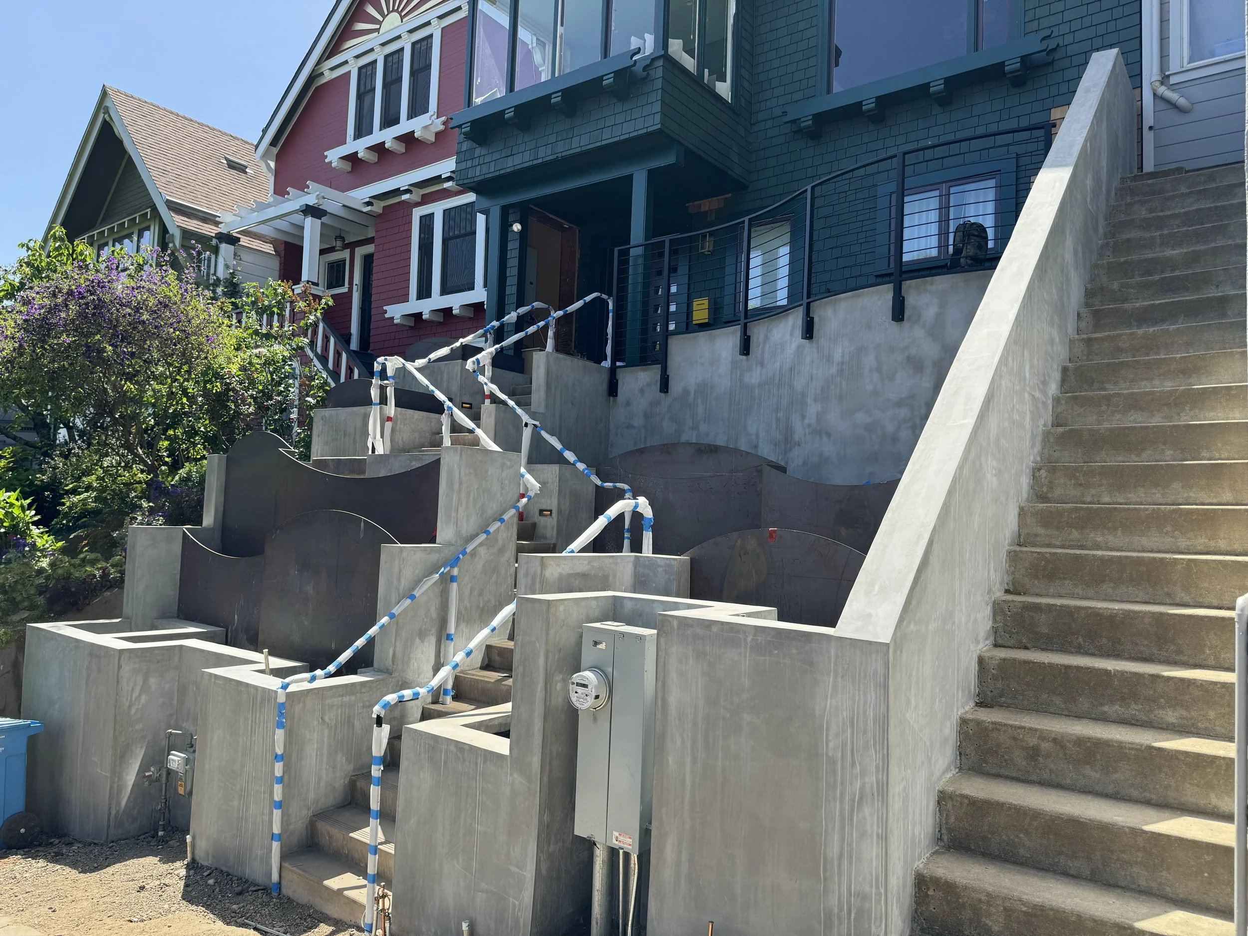 House with newly constructed concrete stairs and terraces, safety tape on railings, and adjacent greenery.