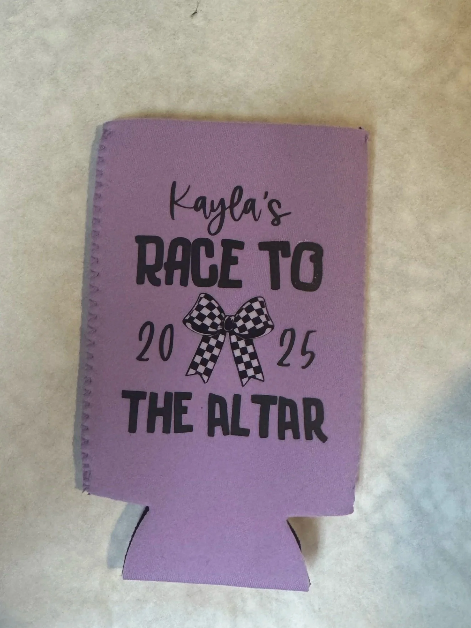 A purple paper ribbon with the text "Kayla's Race to the Altar 2025" and a checkered bow in the center.