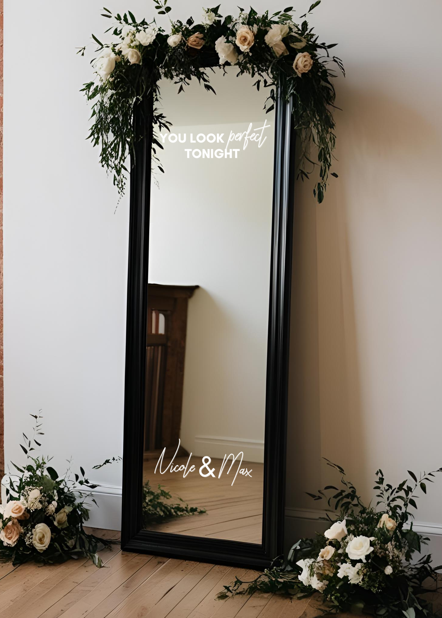 A full-length black-framed mirror decorated with floral arrangements at the top and bottom, displaying the message 'You look perfect tonight' and 'Nicole & Max' in white cursive text.