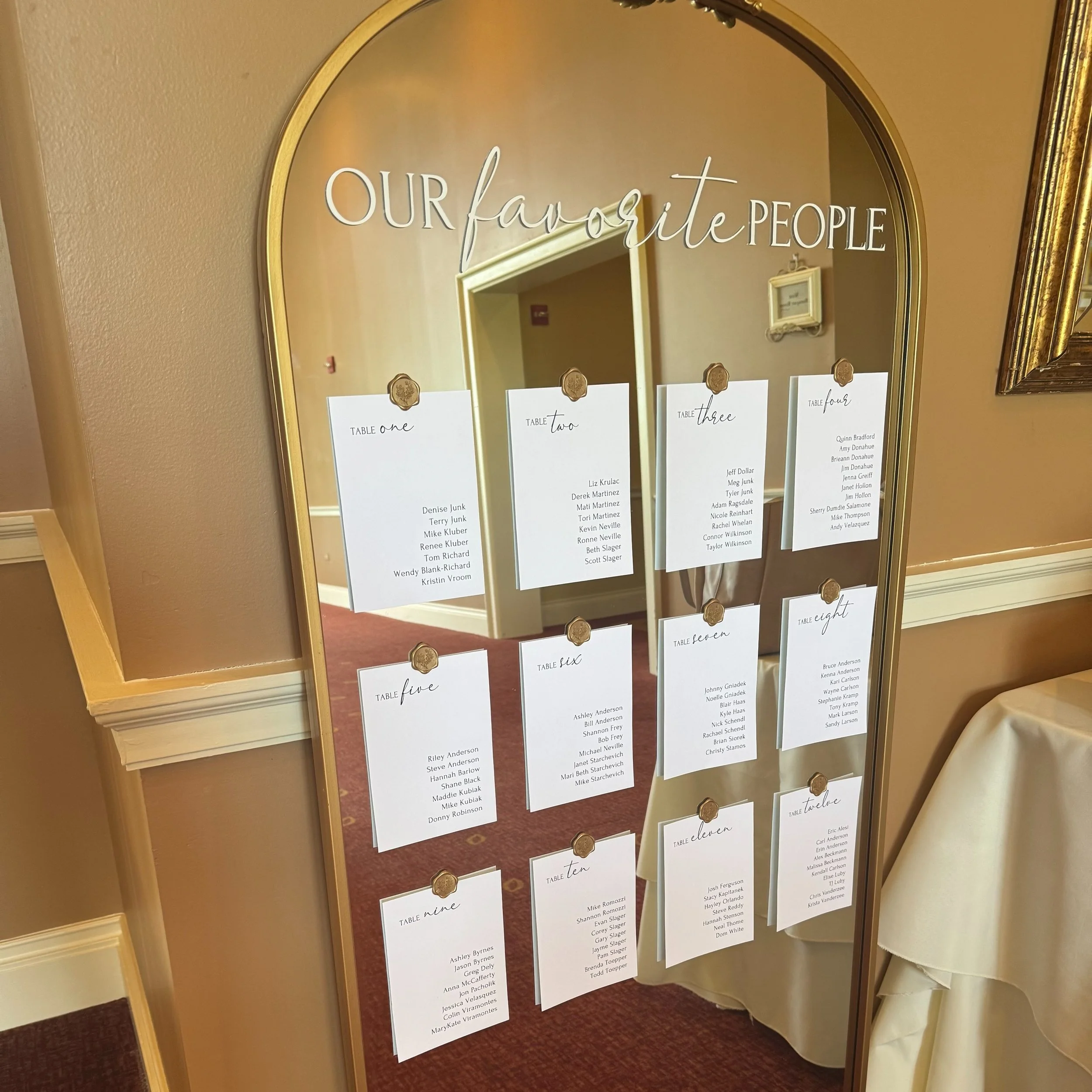 Mirror with seating chart papers clipped to it, titled "Our favorite People", listing tables numbered one to eleven with guest names.