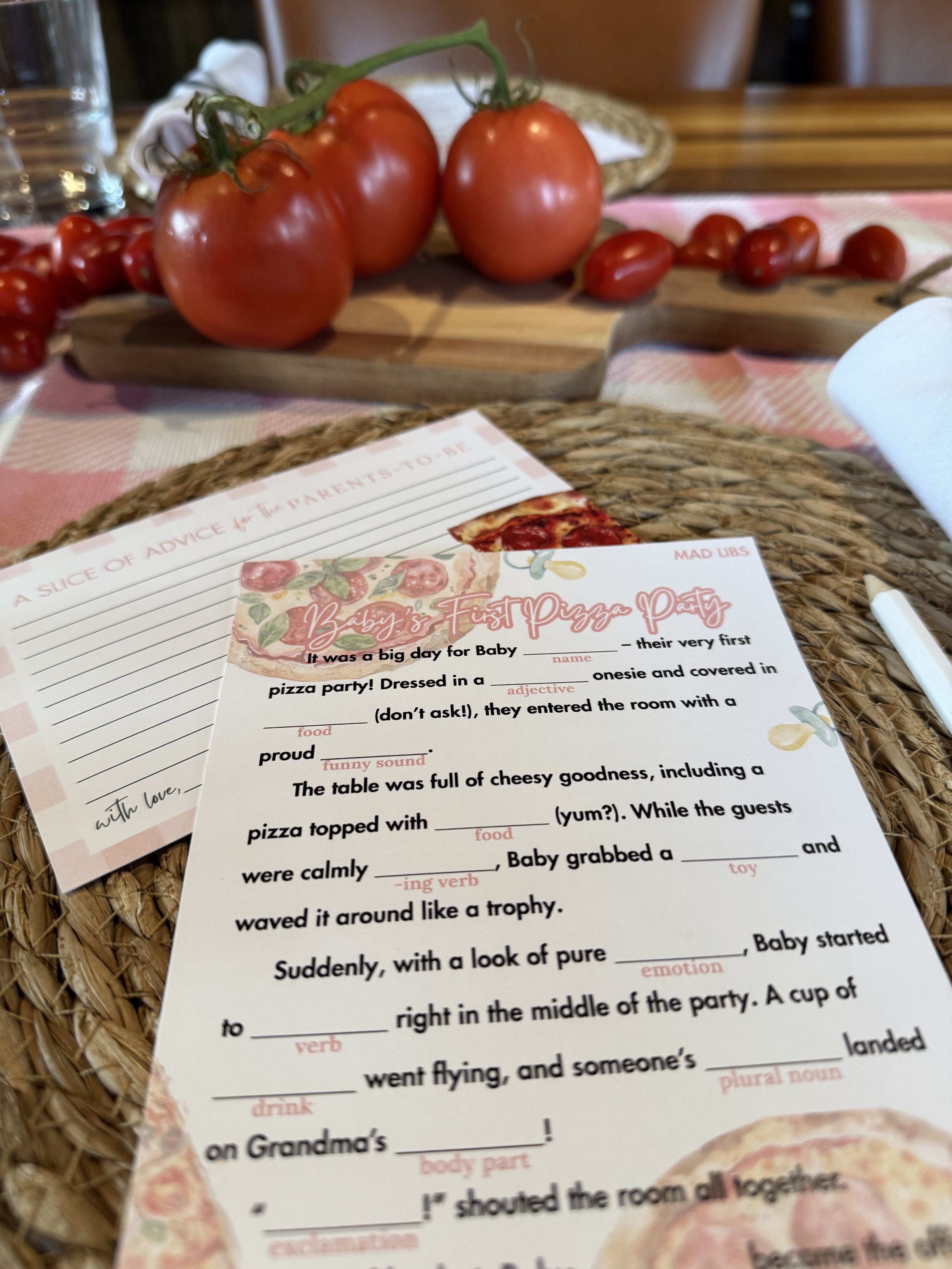 Fresh red tomatoes on a vine and cherry tomatoes on a cutting board in the background, with a pizza-themed activity sheet on a woven placemat in the foreground.
