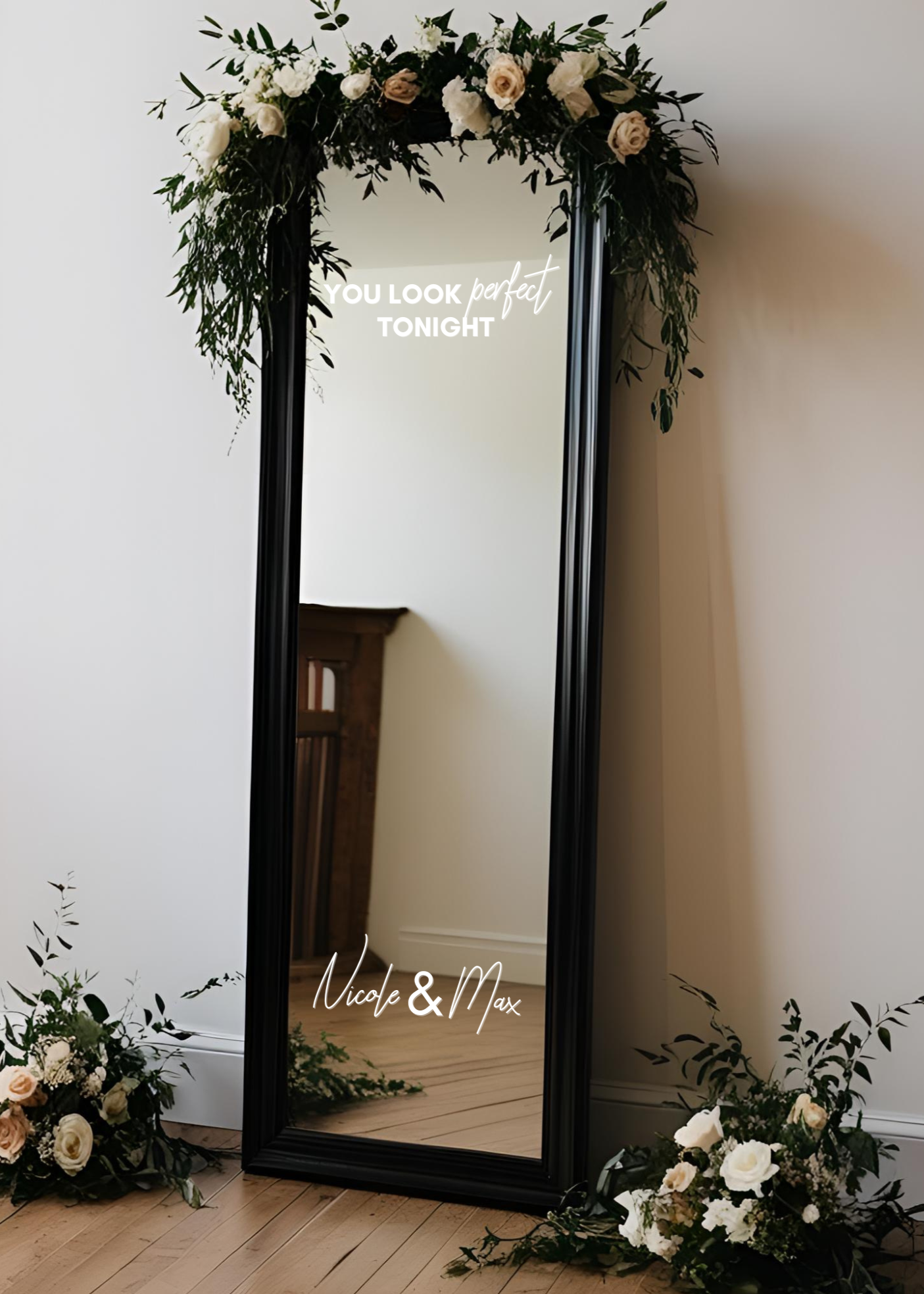 Full-length black-framed mirror decorated with white and cream flowers, greenery, and leaves at the top and bottom, with inspirational text 'You look perfect tonight' and names 'Nicole & Max' written on the mirror.