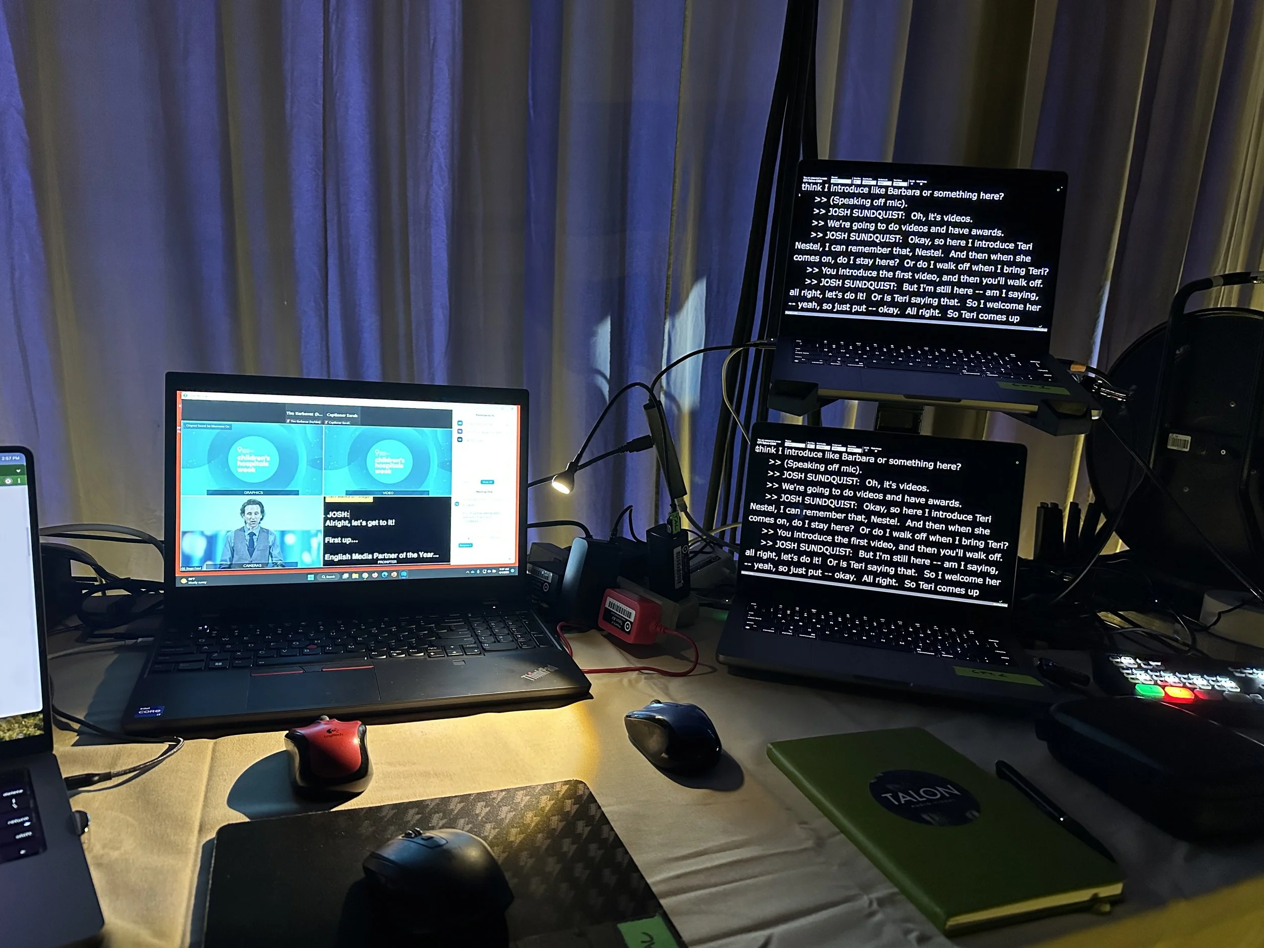 A laptop displays a live video feed while two additional laptops display live captions at a conference.