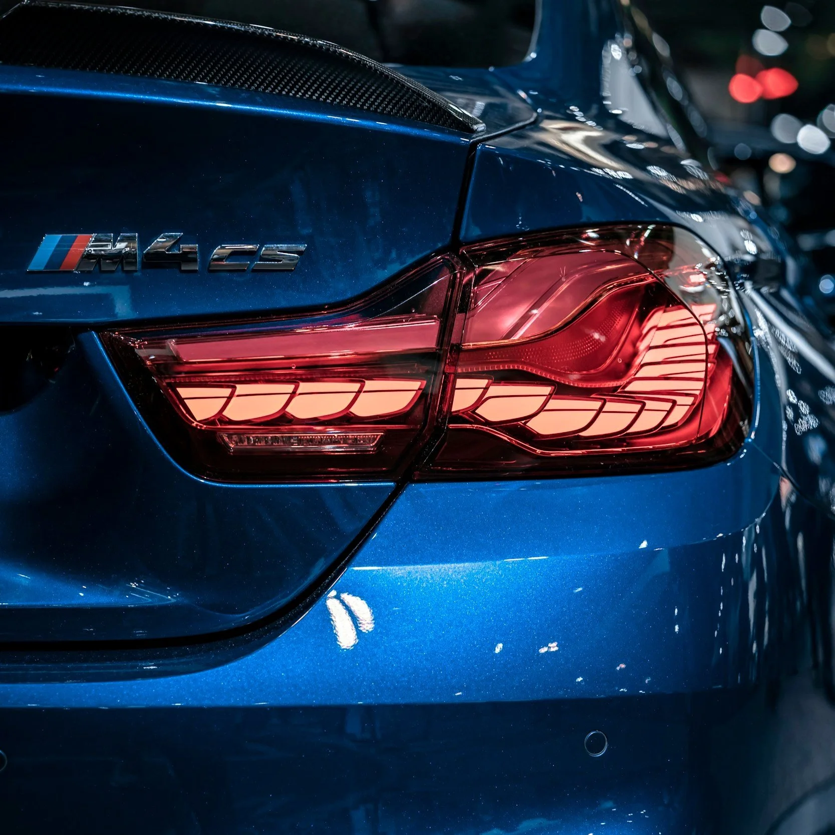 Close-up of the rear section of a blue BMW M4 CS car, highlighting the taillight and M4 CS badge.