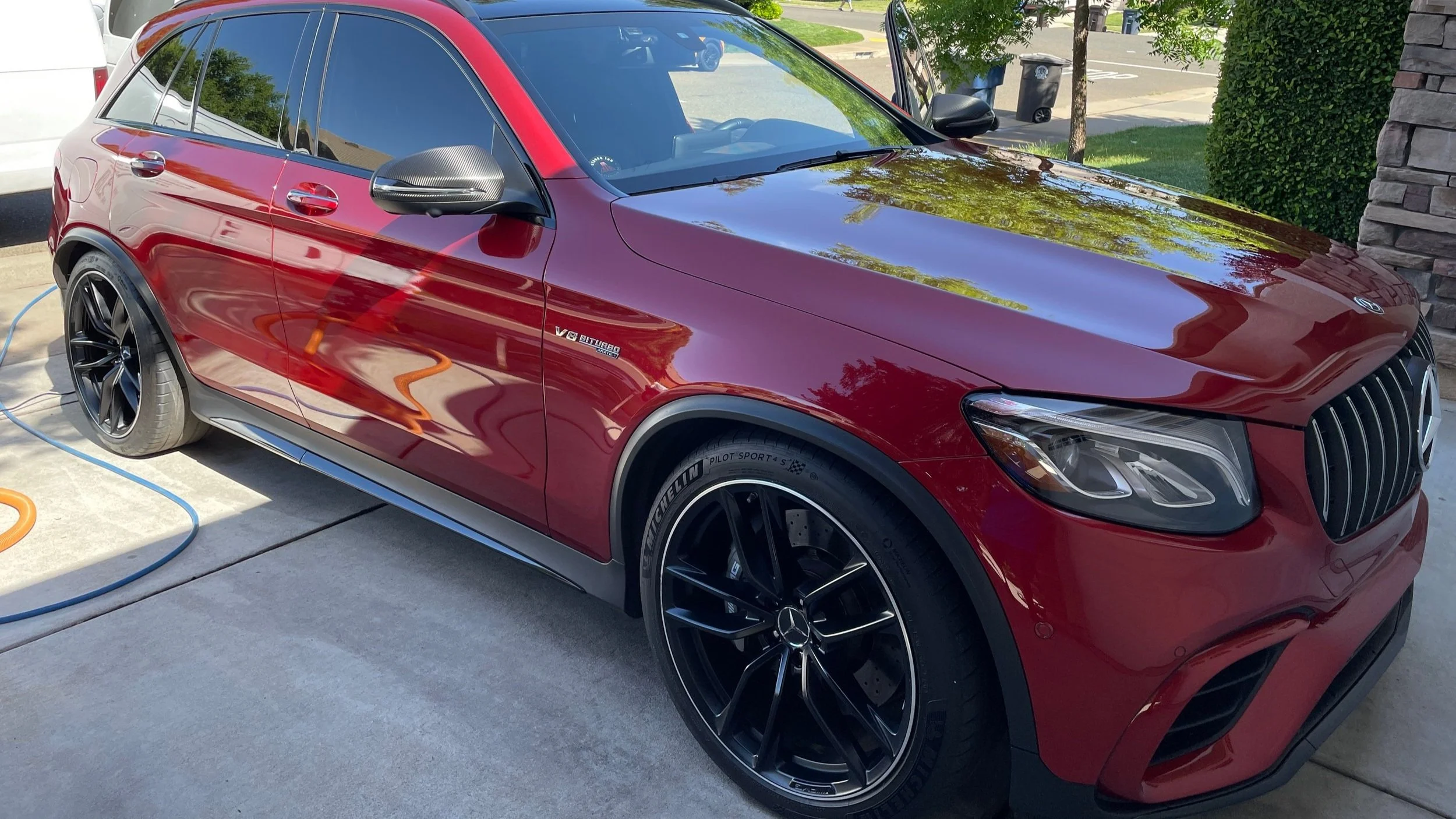 Red Mercedes-Benz SUV parked on driveway, shiny exterior, black alloy wheels, V8 biturbo badge on side, and black carbon fiber side mirrors.