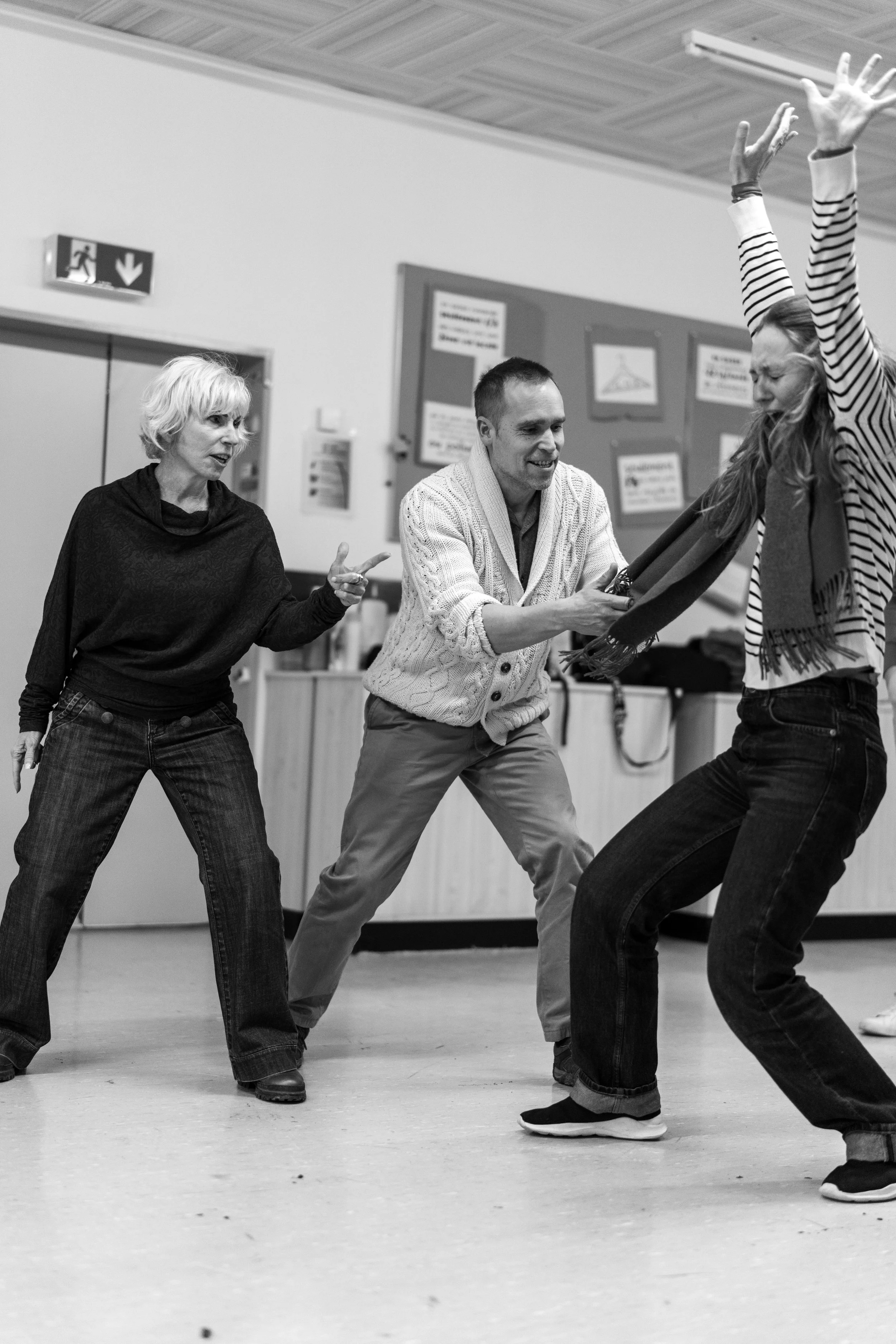 Three people engaged in an expressive activity or performance, indoors, in black and white.