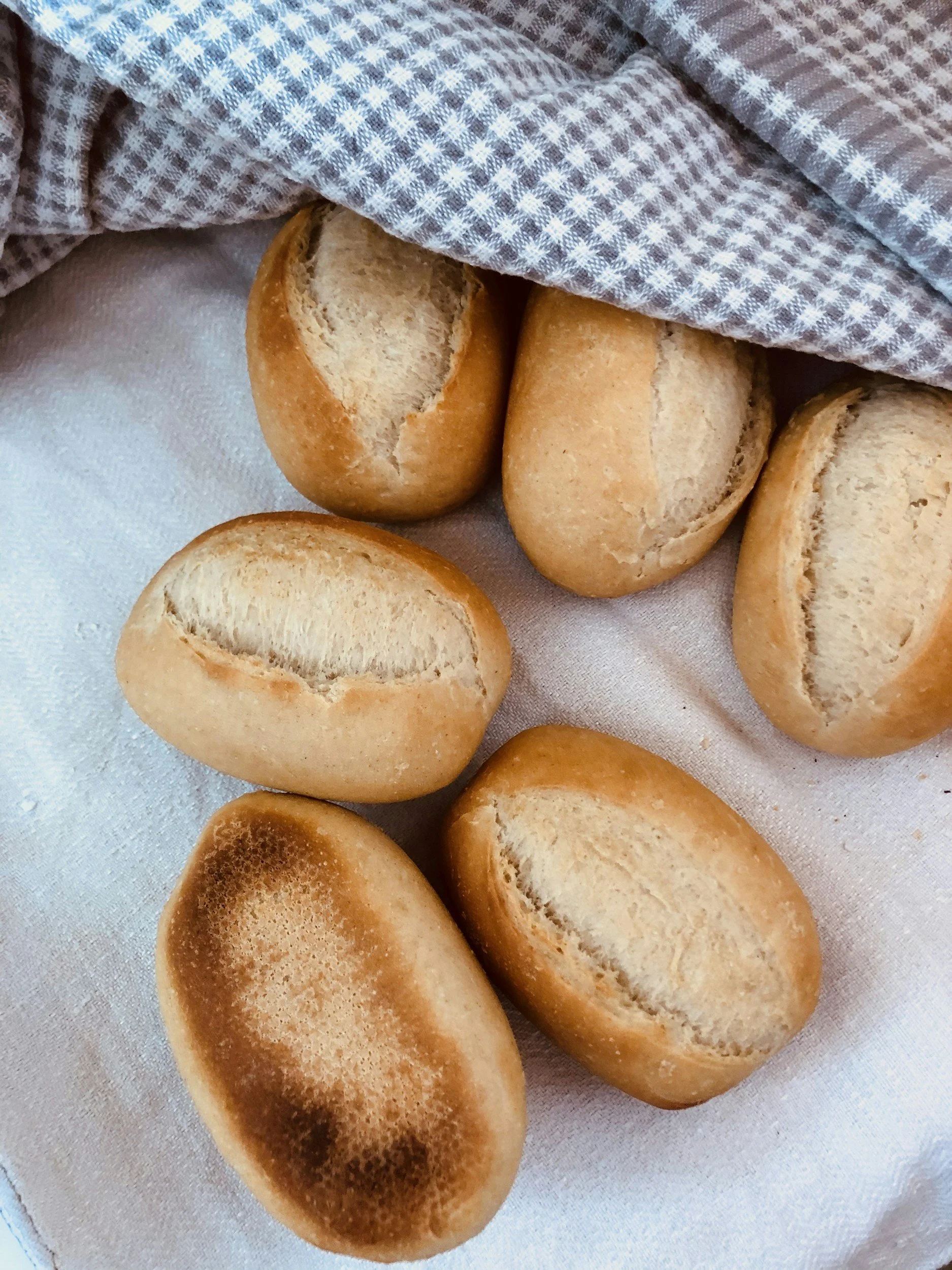 Freshly baked bread rolls on a white cloth, partially covered with a gray and white checkered cloth.