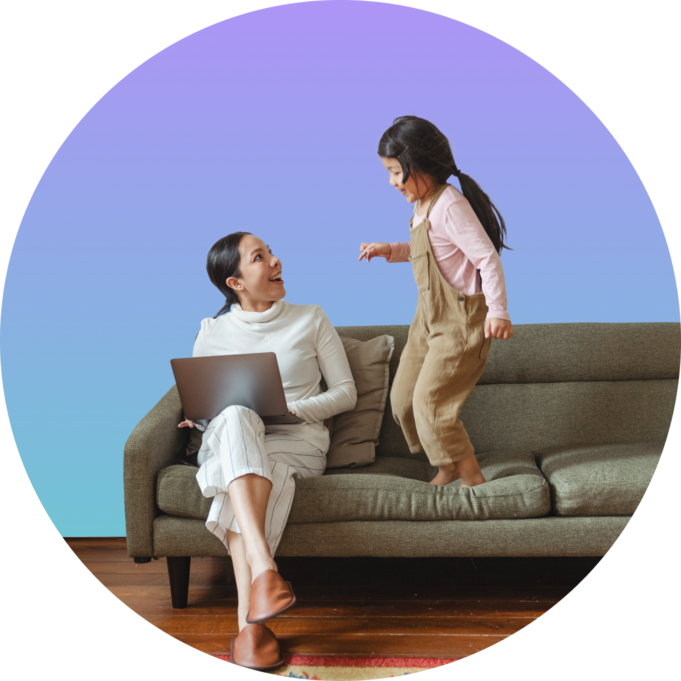 A woman sitting on a gray couch with a laptop, looking up and smiling at a young girl standing on the couch, who is playing or talking animatedly, against a colorful blue-purple gradient background.