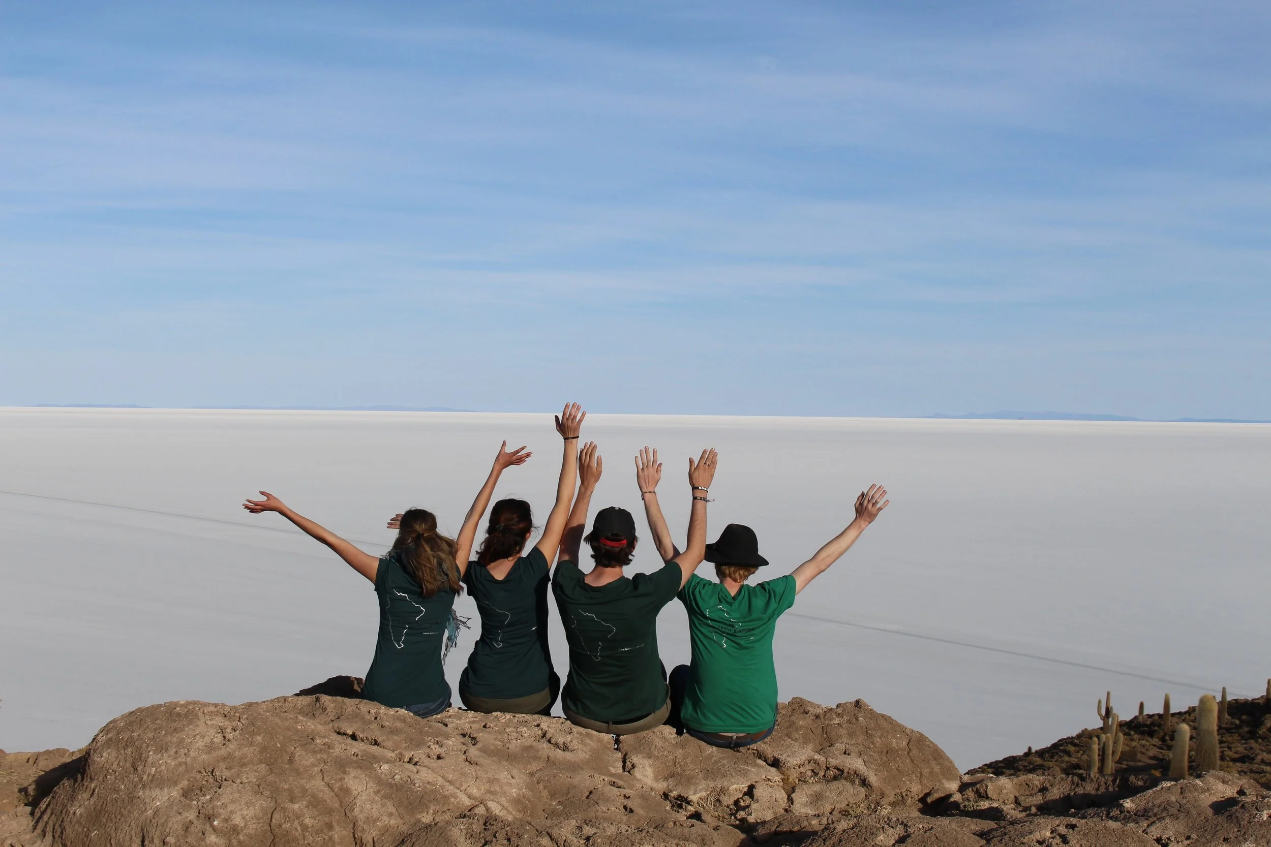 Vier Teilnehmende eines Teameinsatzes in Bolivien – von hinten, Arme in die Luft gestreckt – vor der Salzwüste. Step- und Kurzzeiter berichten von ihren Erfahrungen während ihres Einsatzes in Lateinamerika.