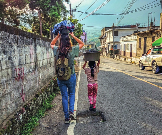 Stay-Mitarbeiterin Murielle von hinten mit einem Mädchen in Guatemala – beide tragen einen Wäschekorb auf dem Kopf. Murielle berichtet, wie sie in ihrem Langzeiteinsatz in Südamerika mit Ungerechtigkeit umgeht.