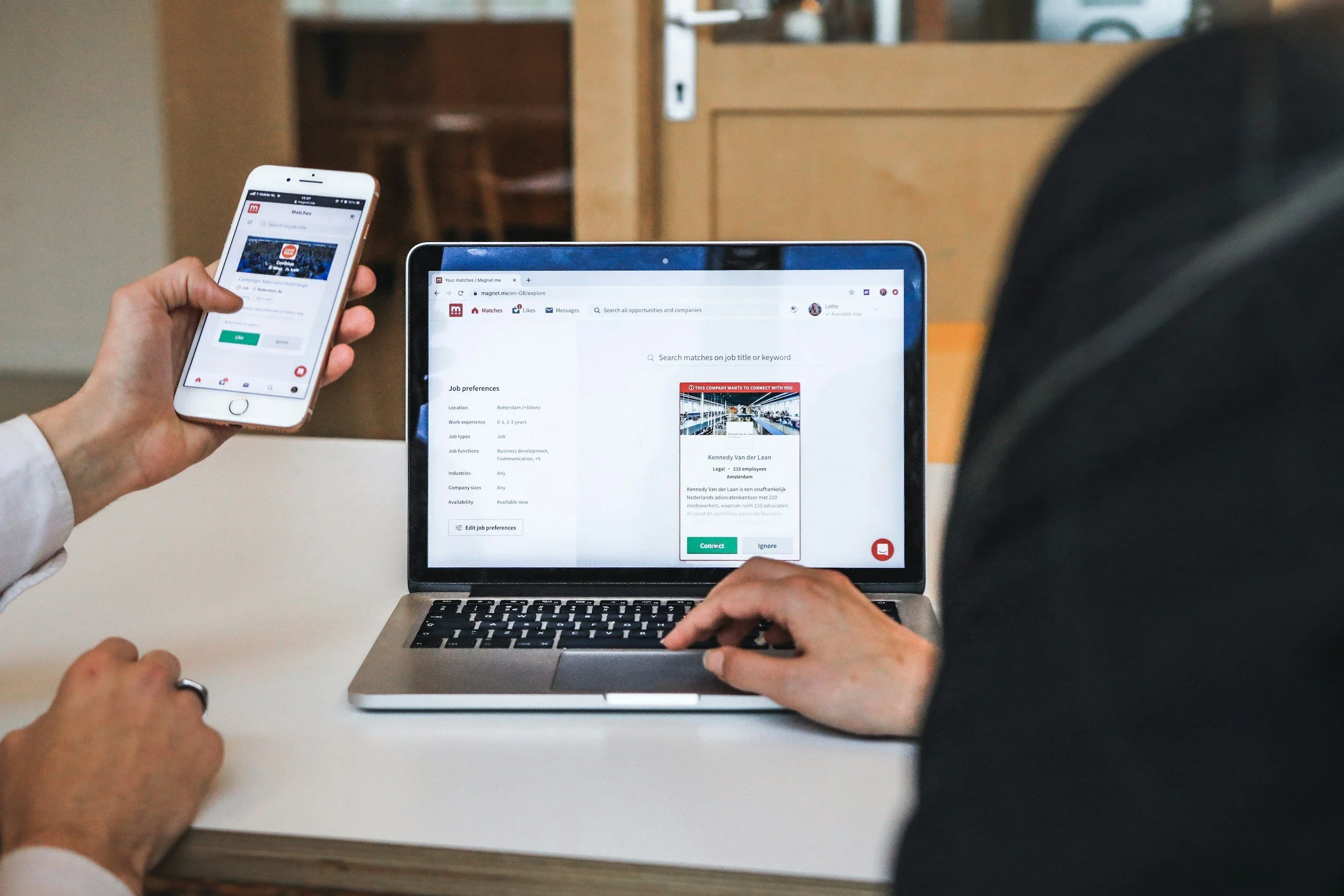 Two people interacting with a laptop and smartphone both displaying job search applications.