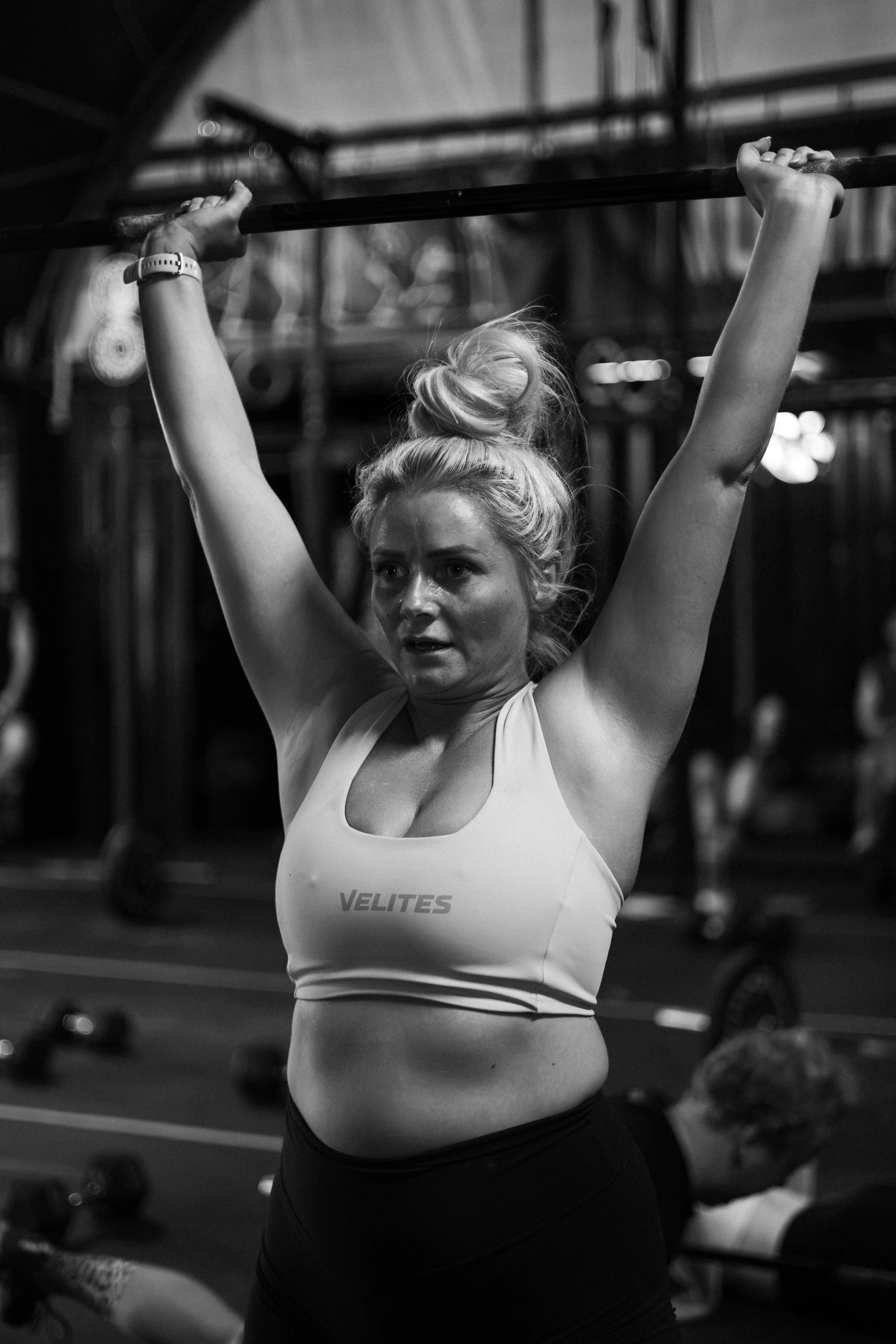 A woman lifting a barbell overhead during a workout in a gym.