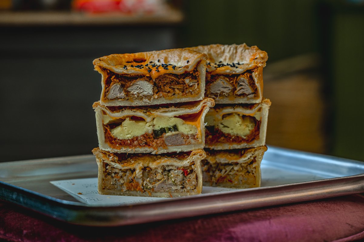 Stack of meat pies with various fillings on a metal tray.