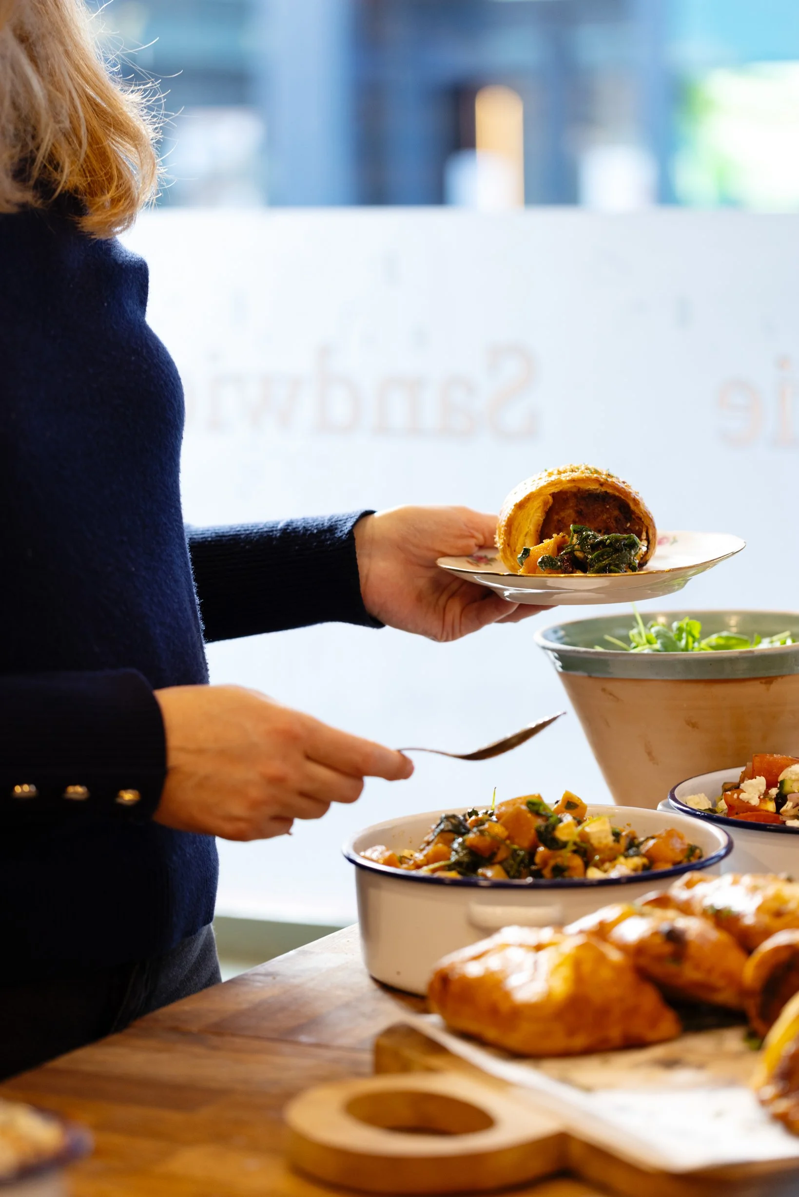 Person serving vegetable-filled pastry onto a plate at a table with various dishes including salads and bread.