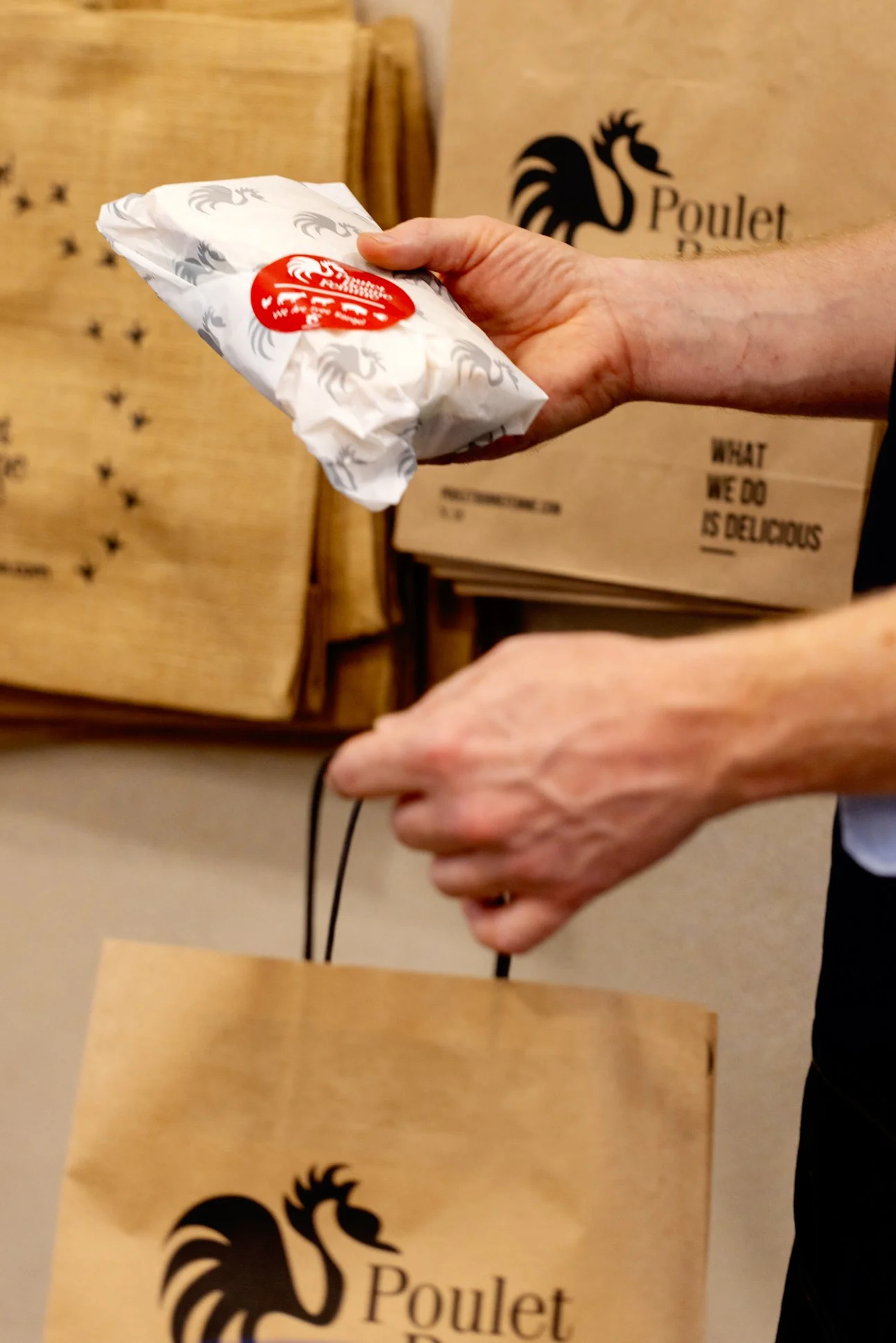 Person holding a wrapped food item in a paper bag with a red logo at a restaurant counter.