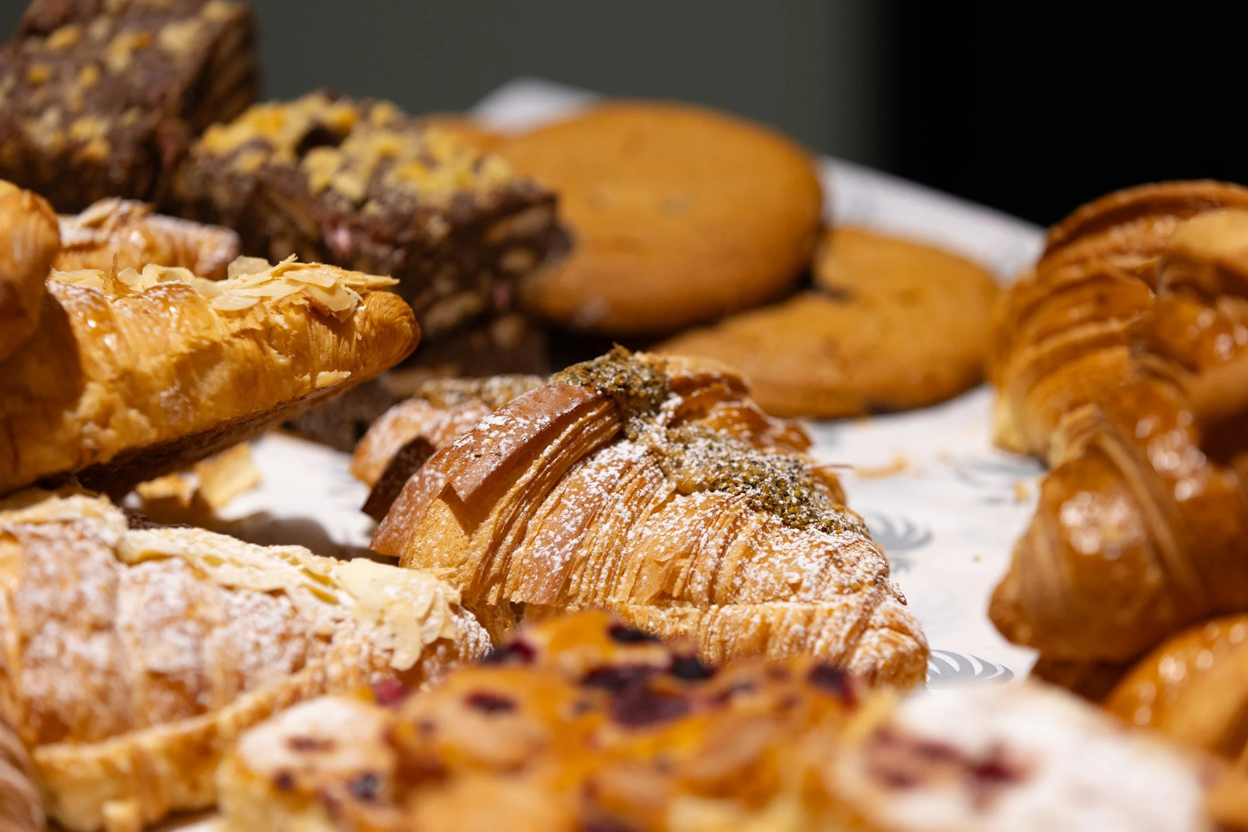 Assorted freshly baked pastries including croissants, cookies, and bars displayed on a tray.