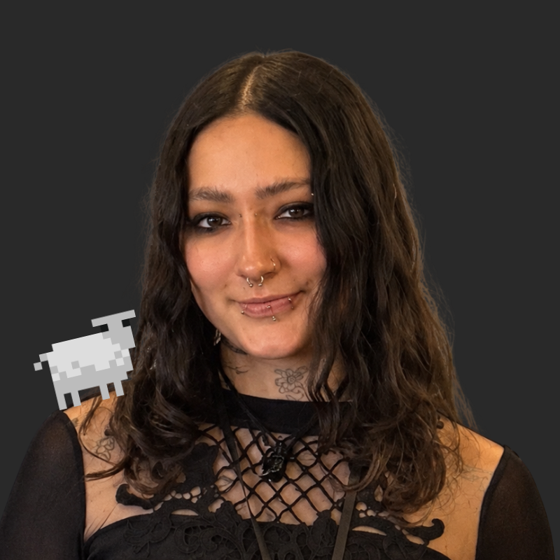 Young woman with wavy dark hair, piercings, tattoos, wearing a black lace top, smiling against a dark gray background, with a pixelated white sheep graphic near her shoulder.