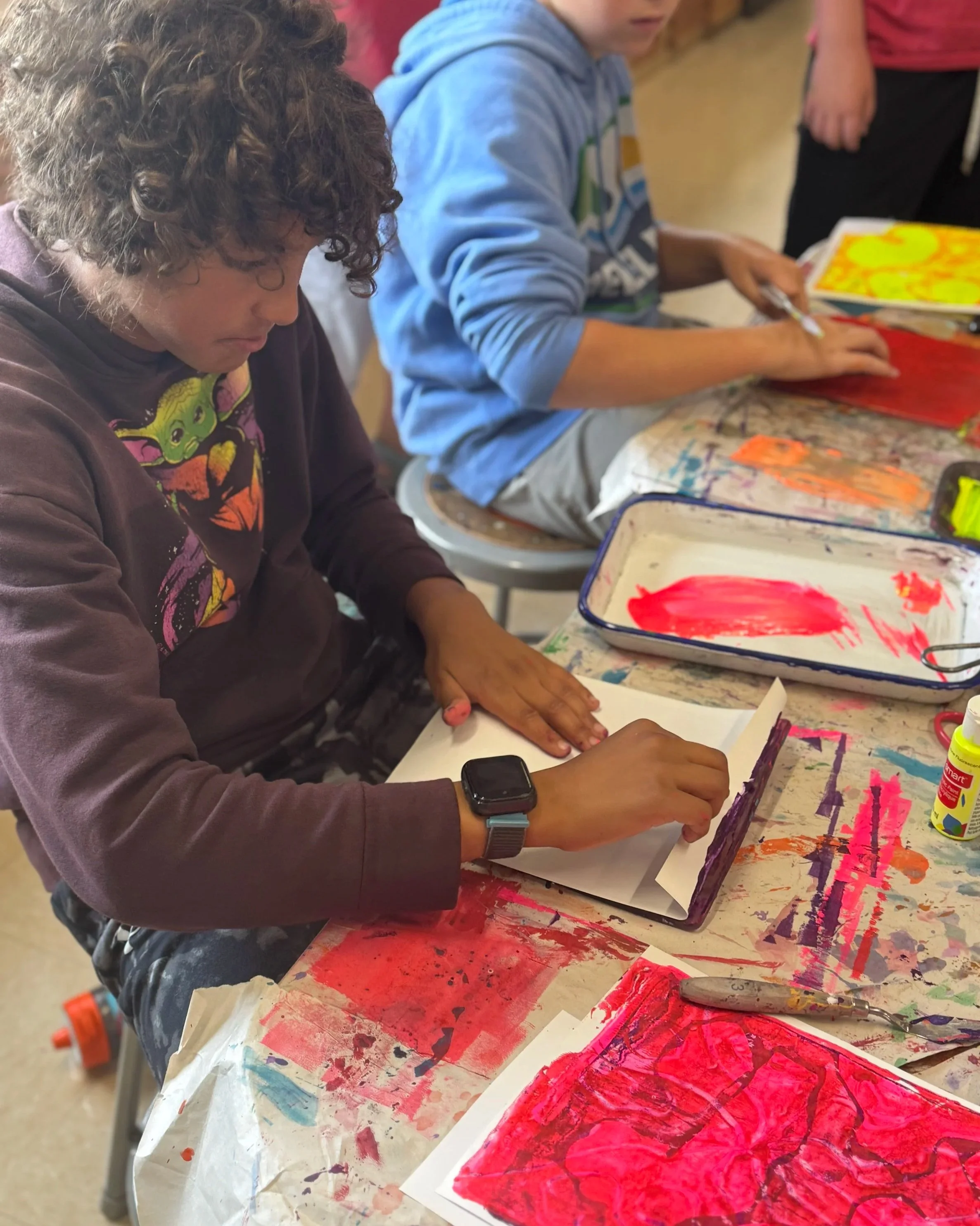 Children creating colorful abstract paintings with paint and paper in an art class.