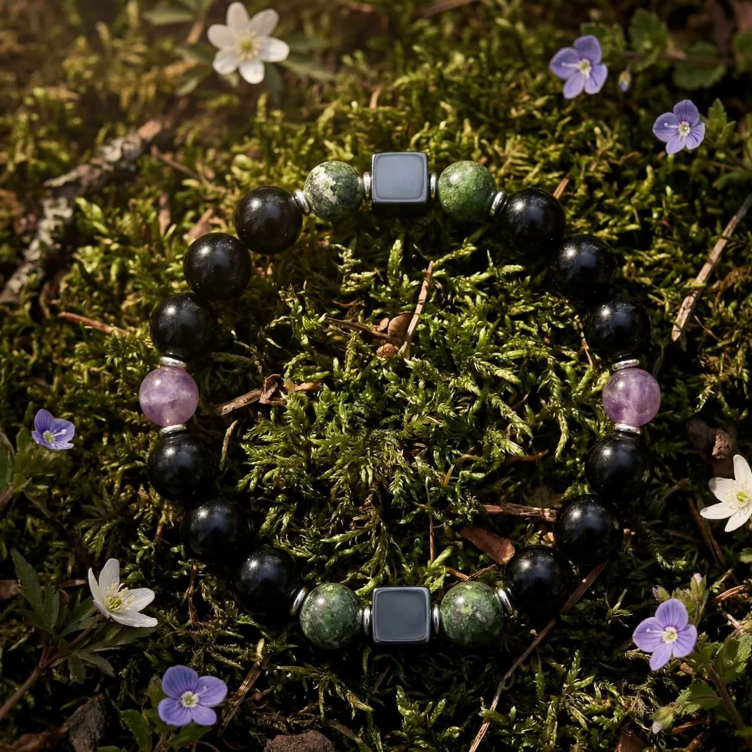 Edelsteinarmband aus schwarzem Obsidian, grünem Diopsid und violettem Lepidolith mit 925 Silber Elementen, arrangiert auf natürlichem Moos mit kleinen Blüten in hochwertiger Naturaufnahme
