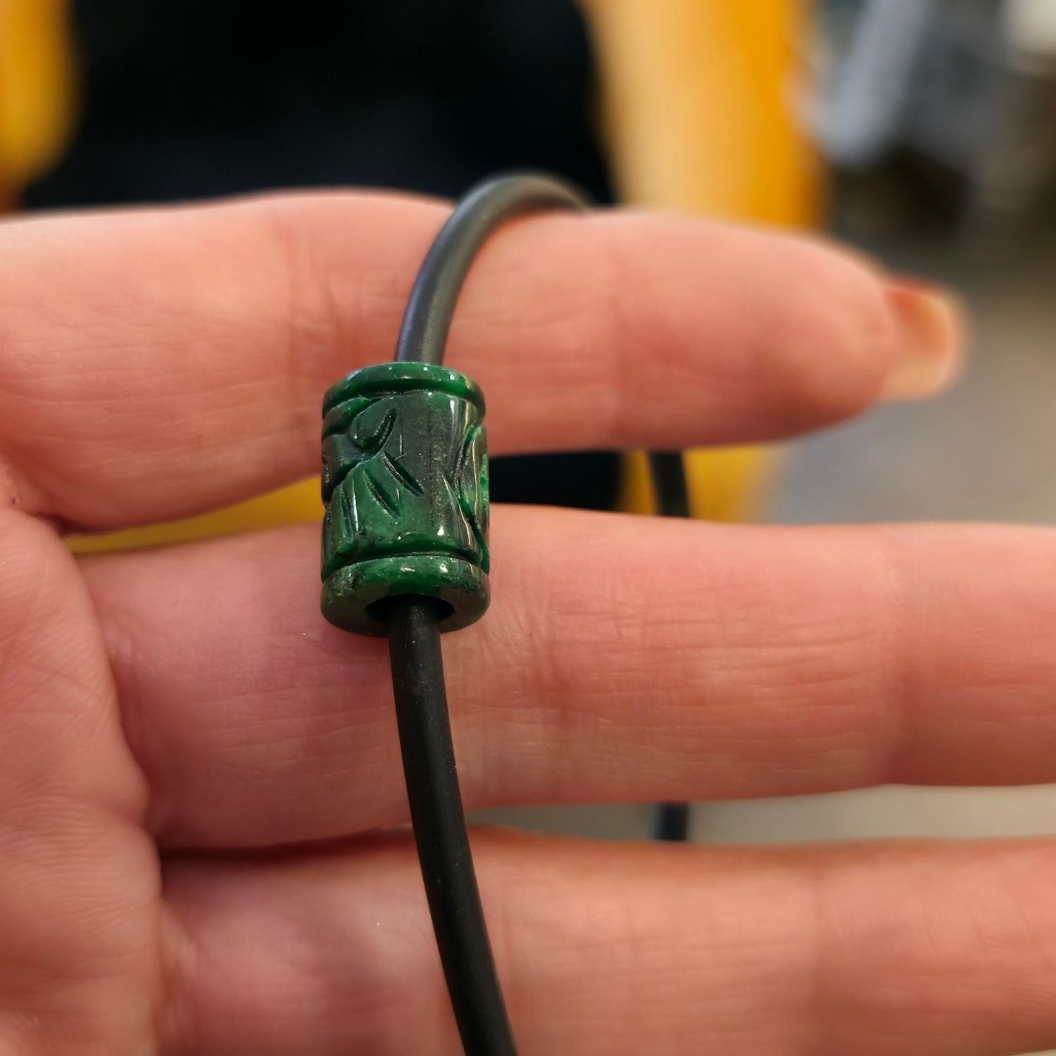 Armband mit handgeschnitztem Burma-Jade-Zylinder auf schwarzem Kautschukband, getragen am Handgelenk, mit 925 Silberverschluss – spiritueller Edelsteinschmuck für Balance und Herzöffnung.