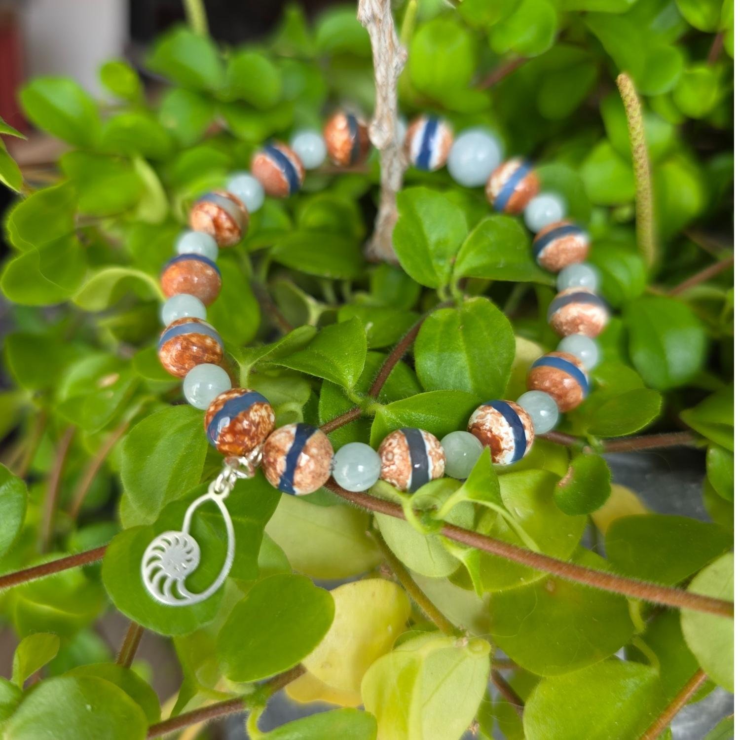 Nahaufnahme des Dzi Achat und Aquamarin Armbands mit Fokus auf die Perlen und das Silber-Schnecken-Symbol