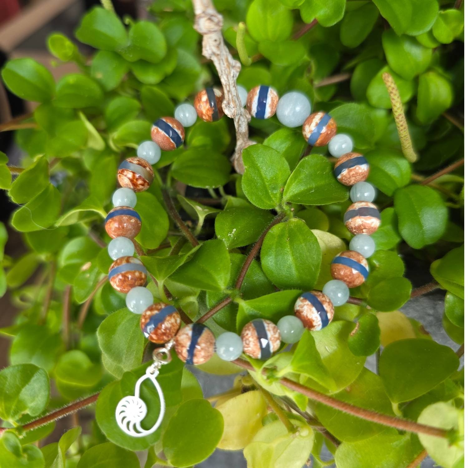 Nahaufnahme des Dzi Achat und Aquamarin Armbands mit Fokus auf die Perlen und das Silber-Schnecken-Symbol