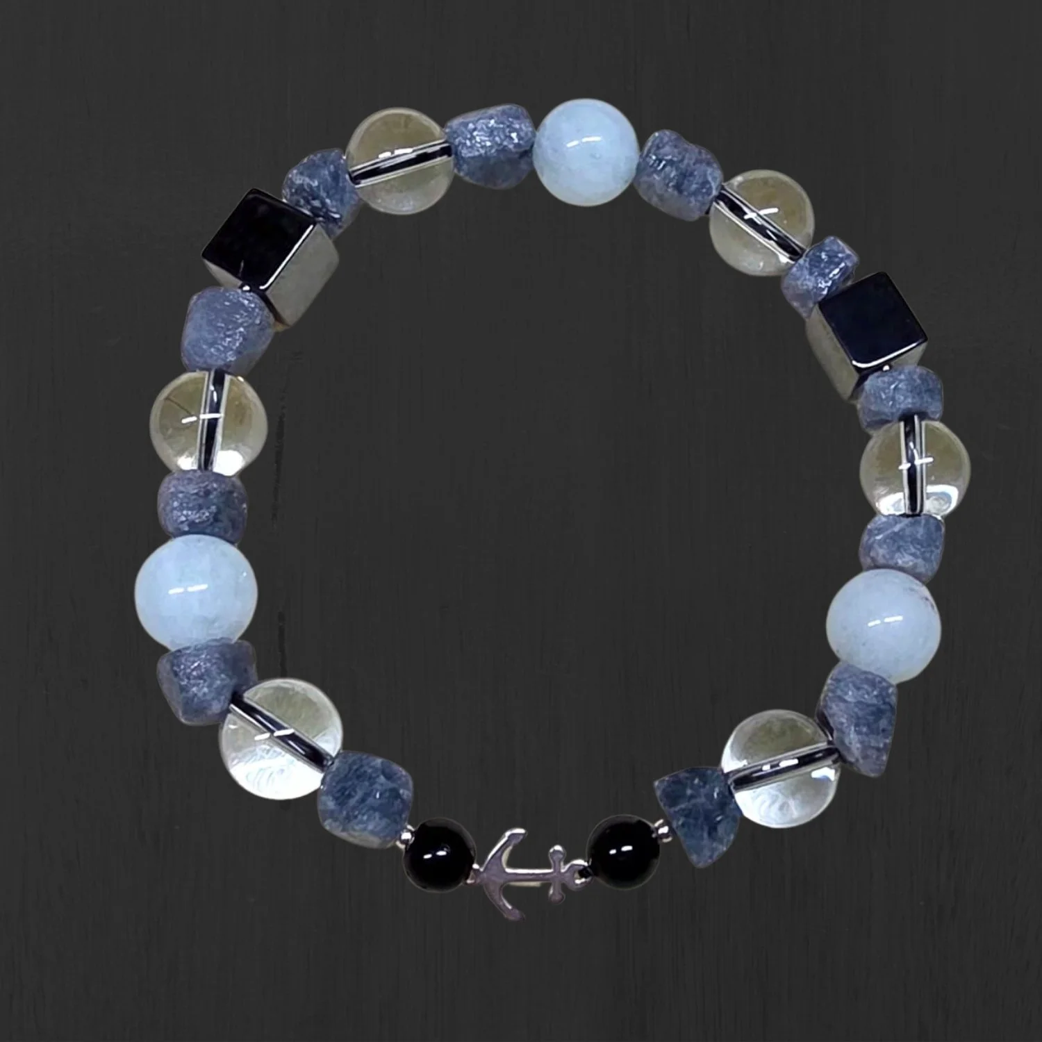 Herrenarmband mit Aquamarin, rohem Saphir, Hämatit-Würfeln, schwarzen Turmalin-Kugeln und 925 Silberanker auf dunklem Hintergrund