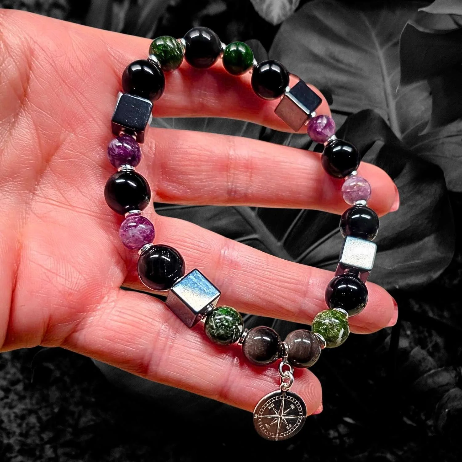 Handgefertigtes Herrenarmband mit Obsidian, Lepidolith, Hämatit und Chromdiopsid sowie 925 Silber Kompass-Anhänger in der Hand gehalten