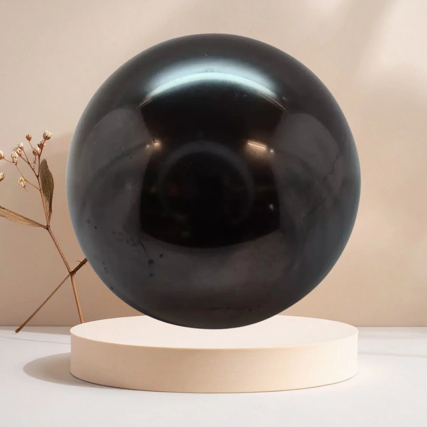 Polierte Schungit Kugel aus schwarzem Naturstein auf hellem Sockel