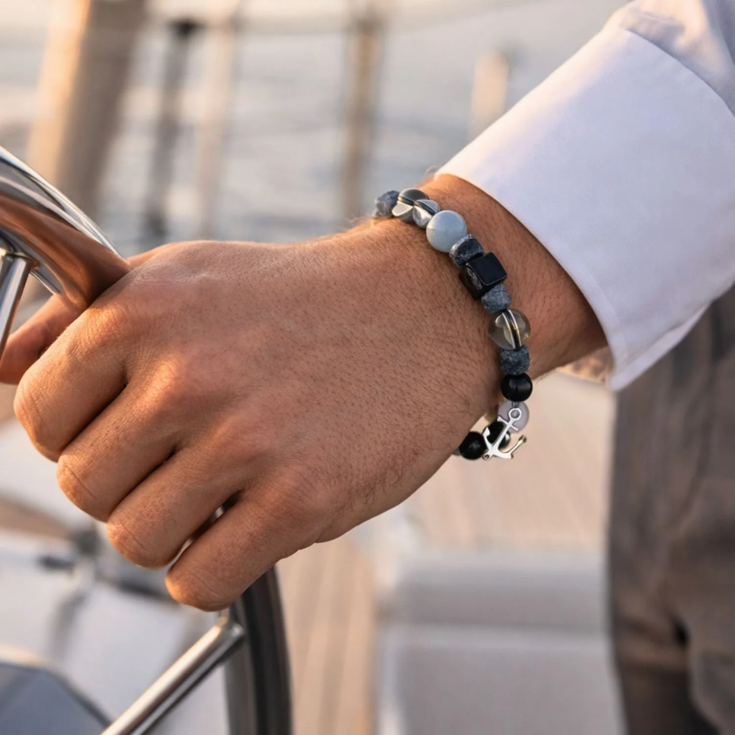 Herrenarmband mit Aquamarin, rohem Saphir, Hämatit und 925 Silberanker am Handgelenk auf einer modernen Segelyacht