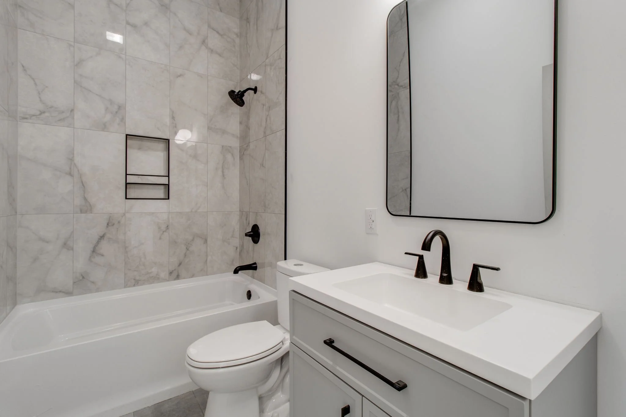 Modern bathroom with marble tiles, bathtub, vanity with sink, and wall-mounted mirror.